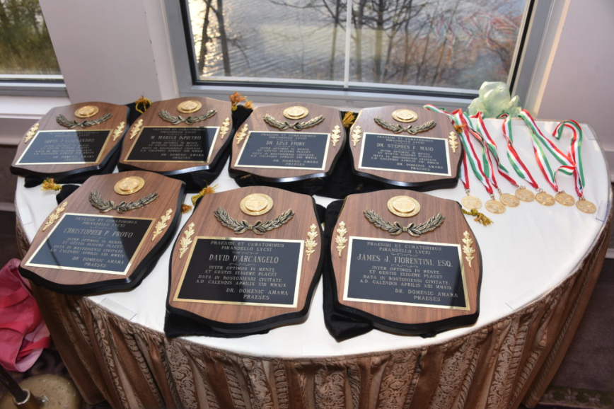 A table displaying several awards and medals, including plaques with gold and silver wreaths and ribbons with medals, set on a white tablecloth near a window.