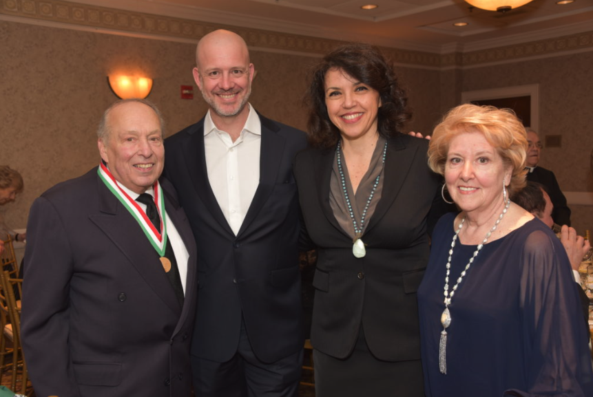 Four people dressed in formal attire standing together at a formal event or celebration, smiling at the camera.