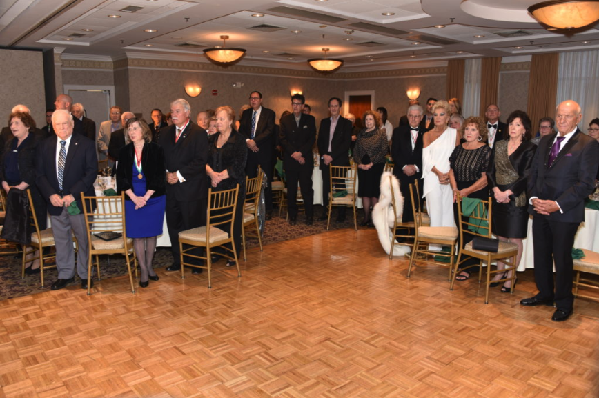 A group of formally dressed people standing in a banquet hall during a formal event or ceremony.