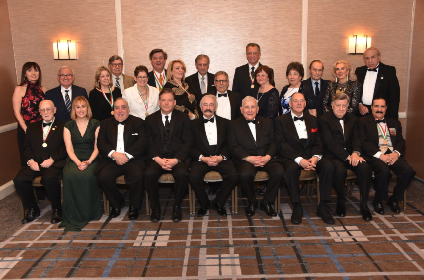 Group of men and women dressed in formal attire, some with medals and ribbons, posing for a photo at a formal event or awards ceremony.