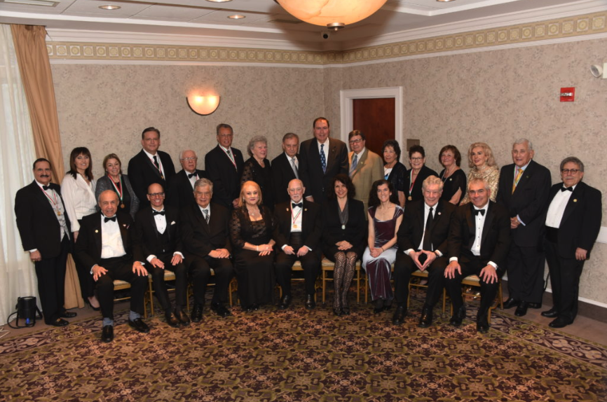 Group of men and women dressed in formal attire, gathered in a banquet or conference room for a professional or celebratory event.