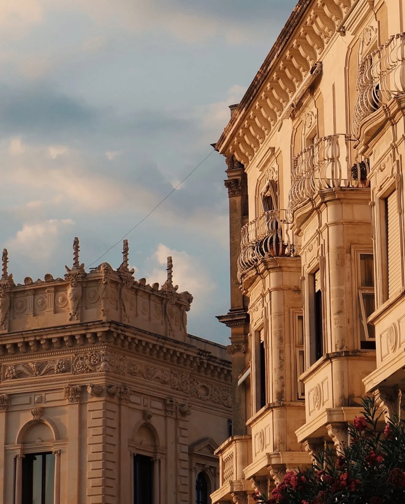 Close-up of ornate, historic European-style buildings with detailed stone facades and small balconies, under a partly cloudy sky. Baroque style building in Siracusa, Sicily