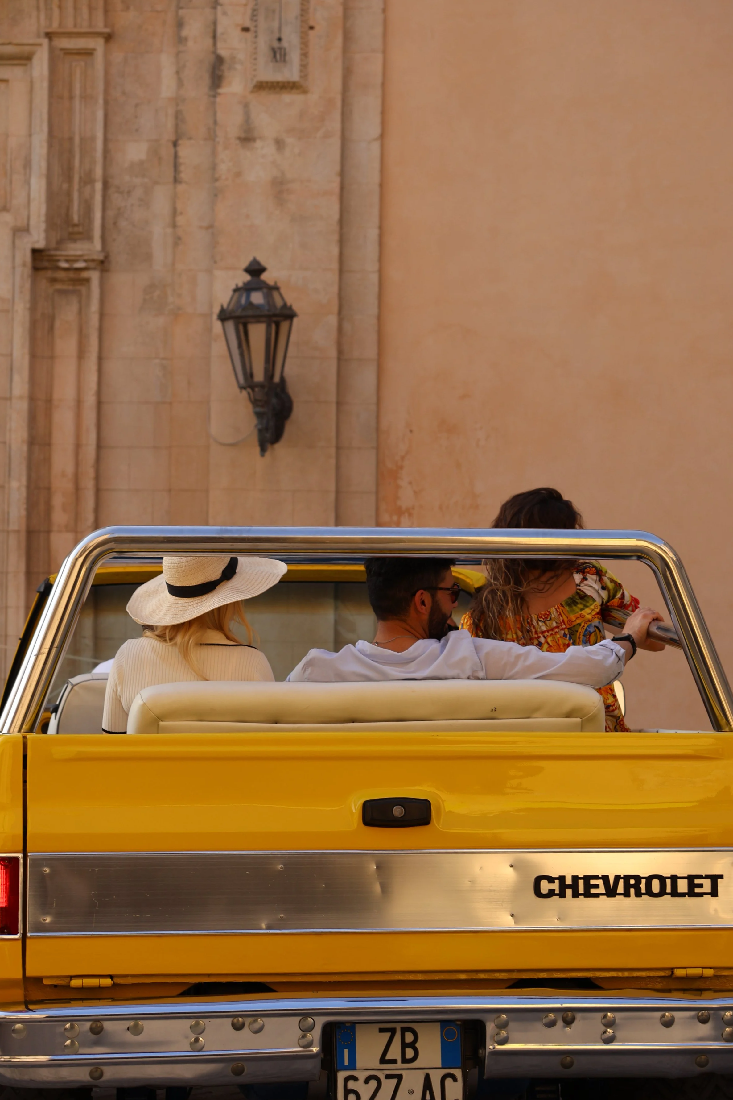 People riding in a yellow Chevrolet vintage convertible car on a street.