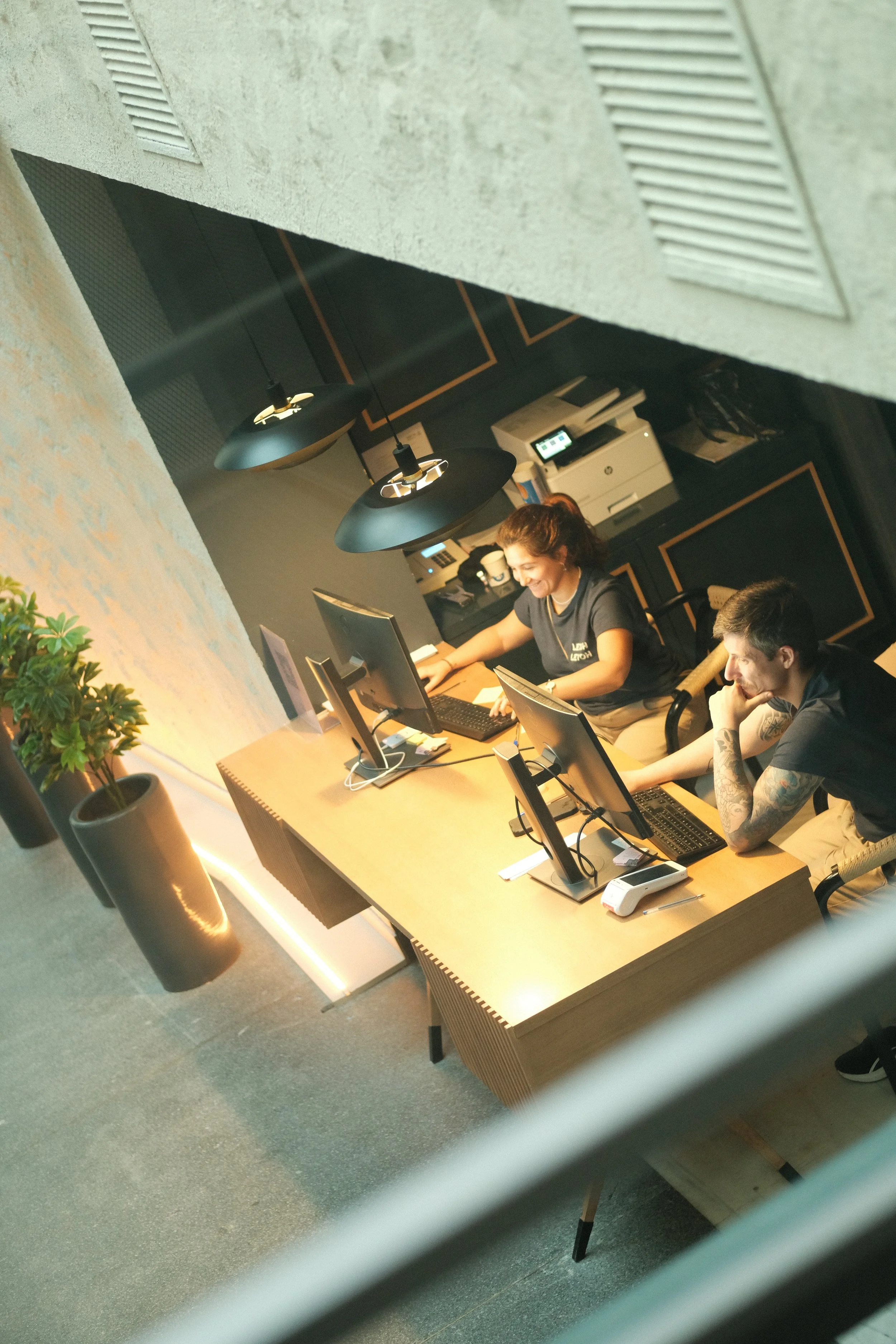 Two women sitting at a reception desk with computers, smiling and working in an office.