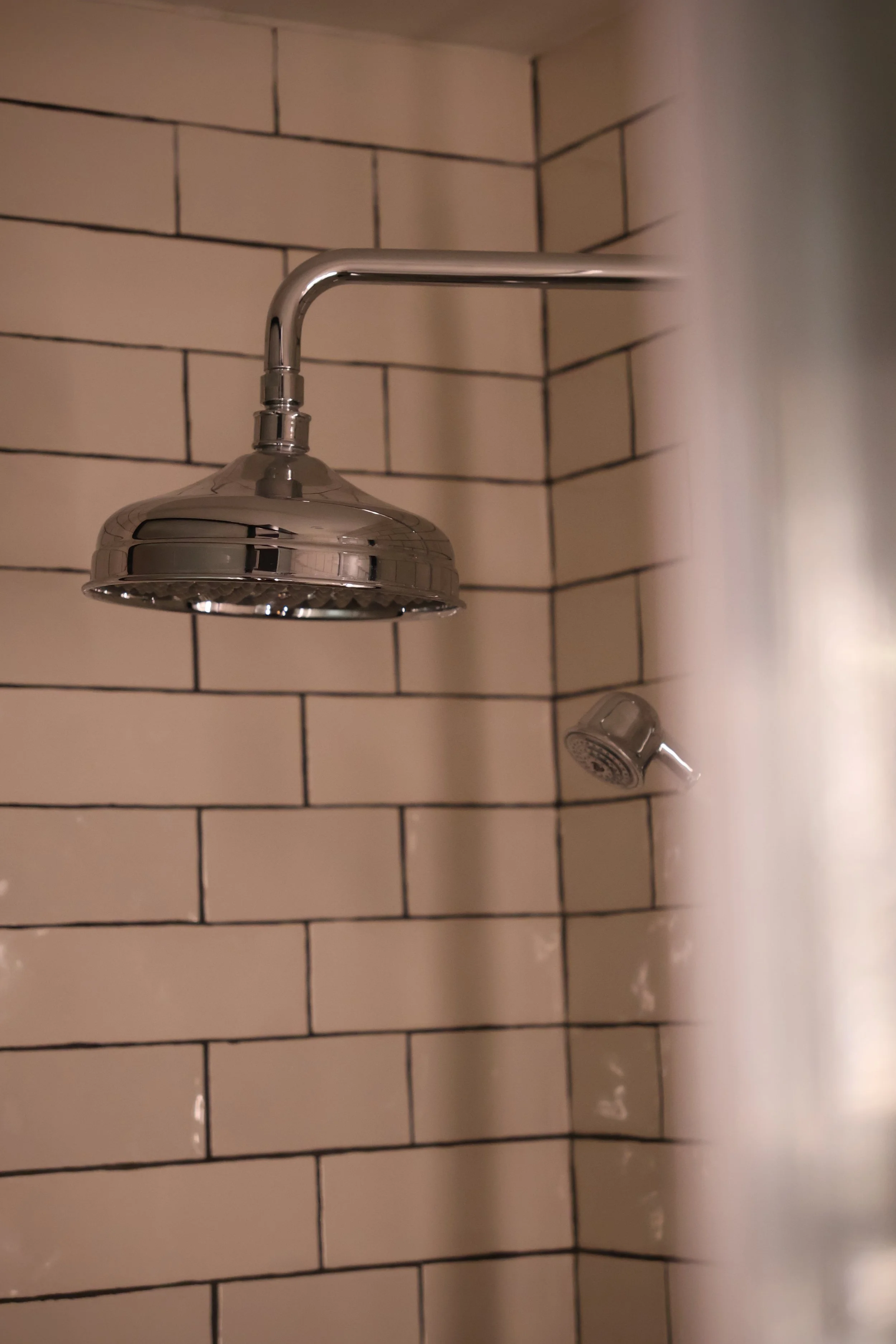 A chrome showerhead and a small handheld showerhead mounted on a tiled bathroom wall.
