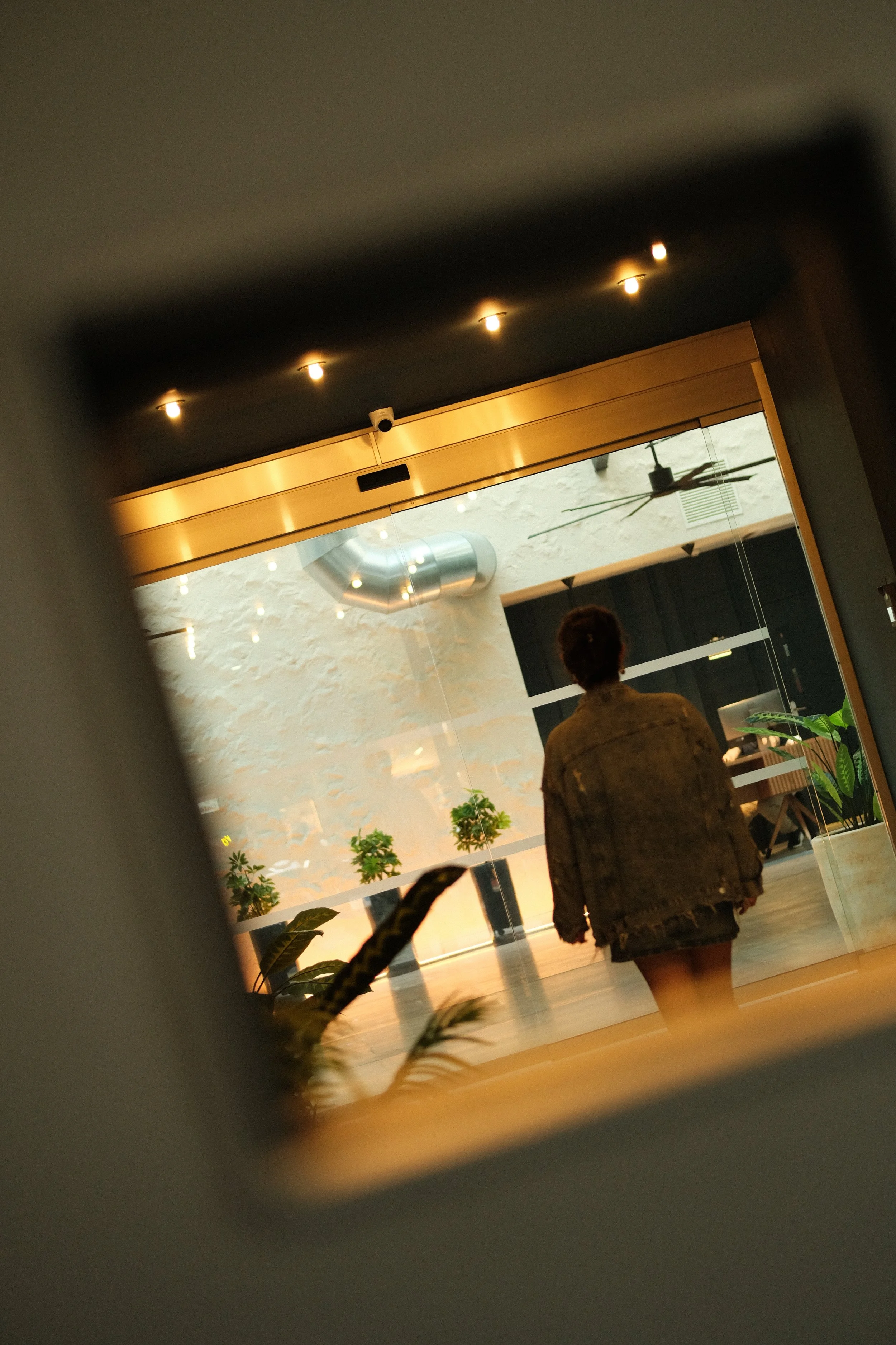 A person walking into a modern indoor space through a glass door, with plants and industrial-style decor visible.