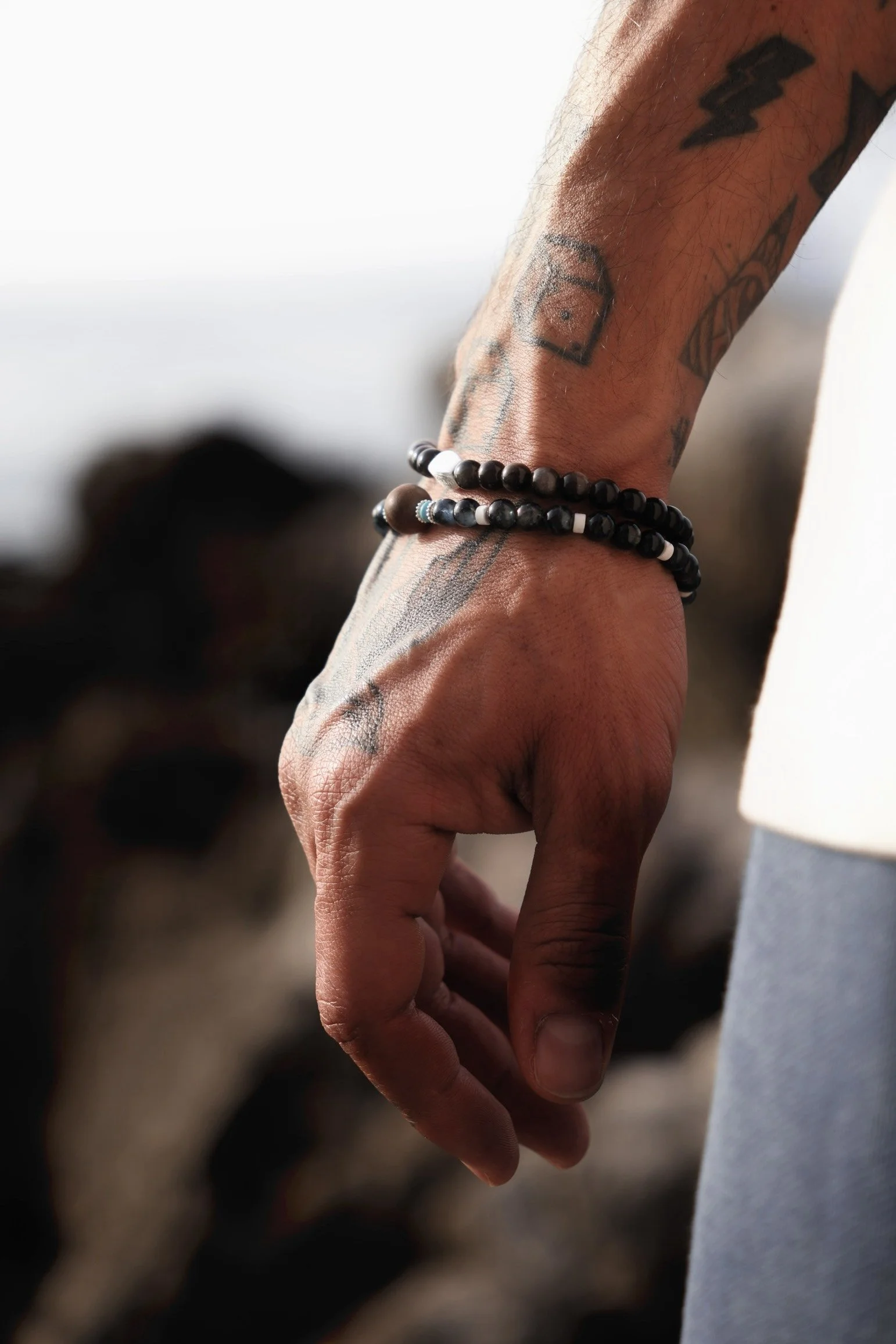 Editorial foto for men's fashion. Close-up of a person's hand and wrist, with tattoos and beaded bracelets, hanging down.