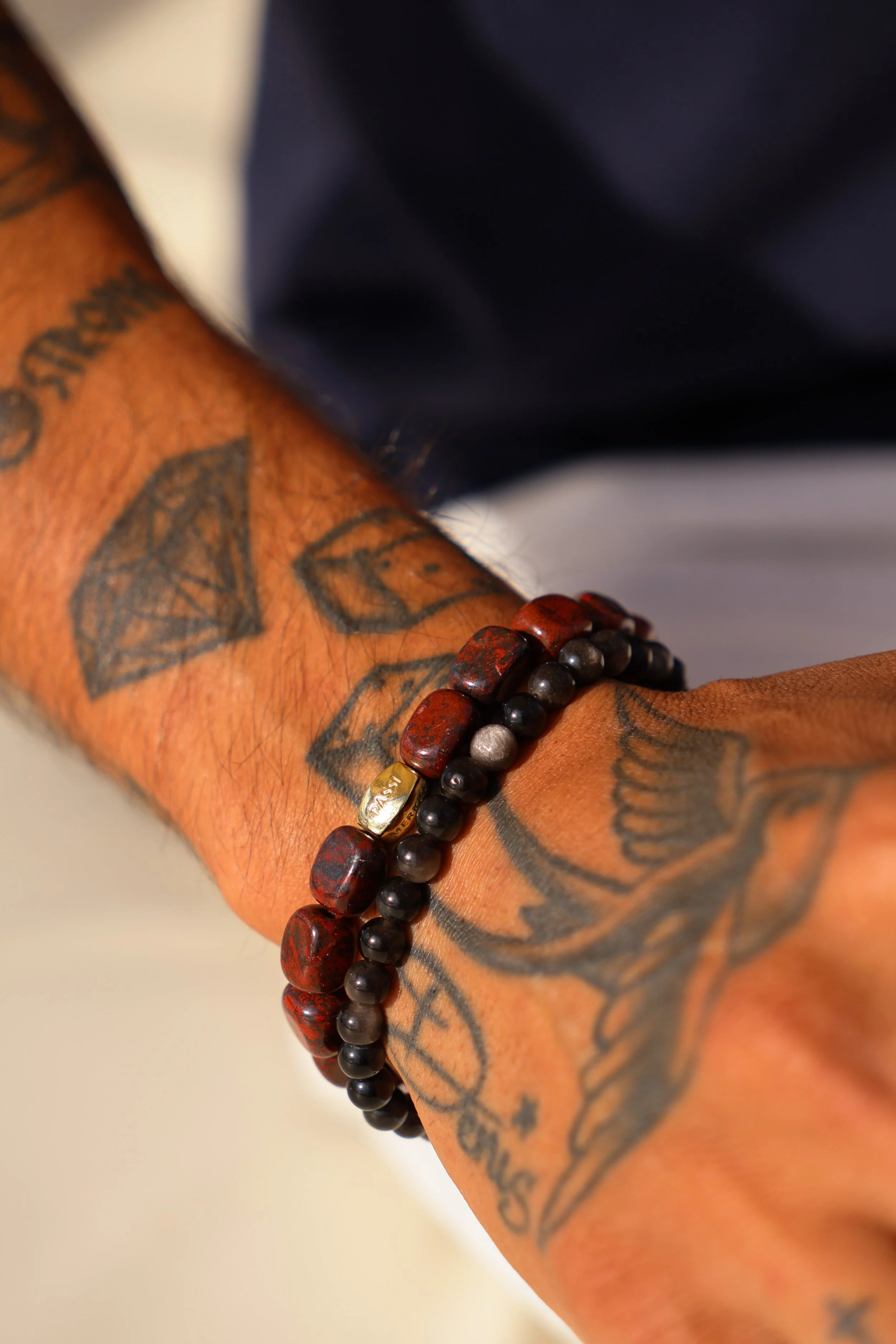 A person's arm with tattoos and a beaded bracelet.