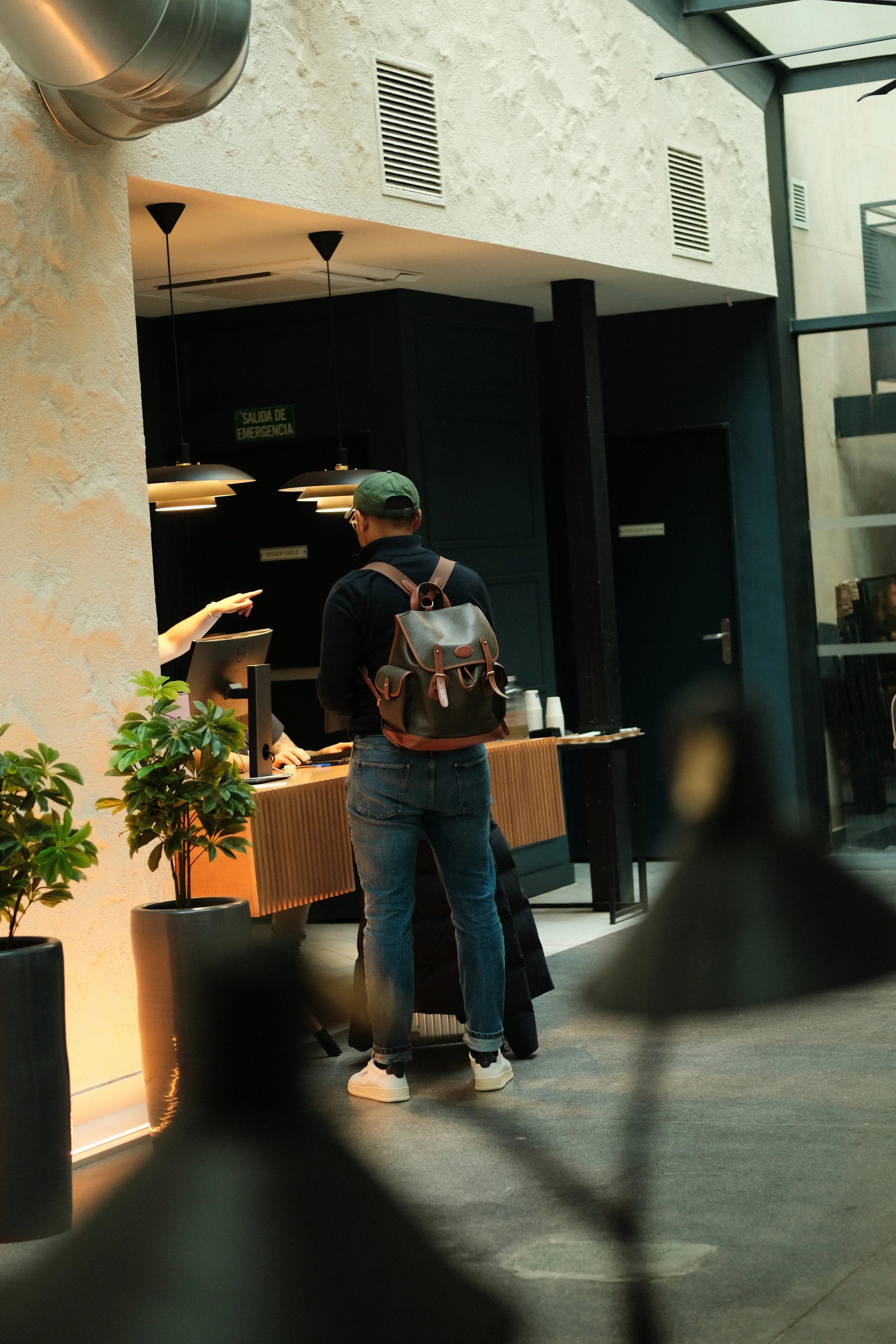 A person with a backpack standing at a counter, interacting with staff at a coffee shop or reception area.