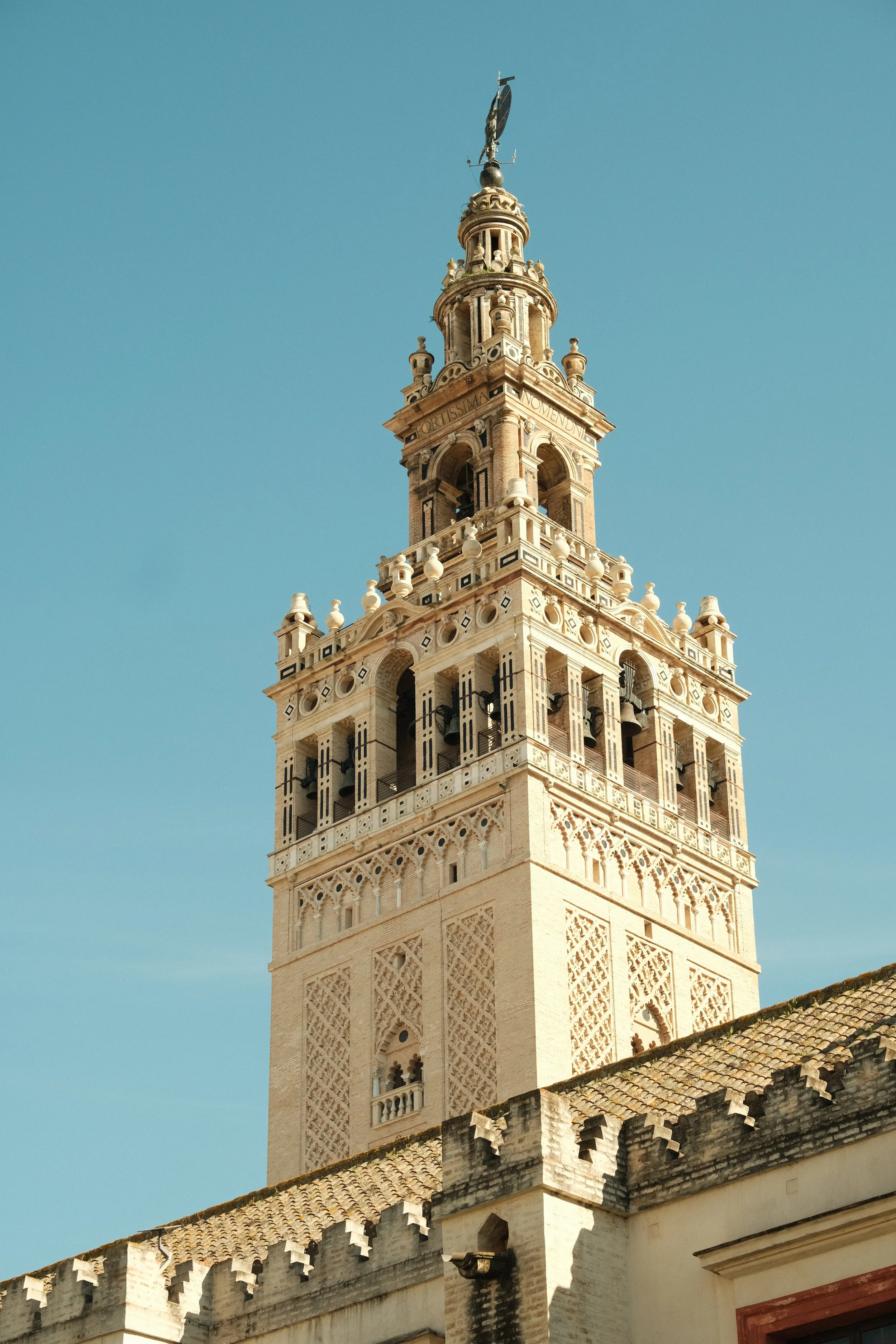 A tall historic bell tower with intricate architectural details against a clear blue sky, featuring arched windows and decorative elements.