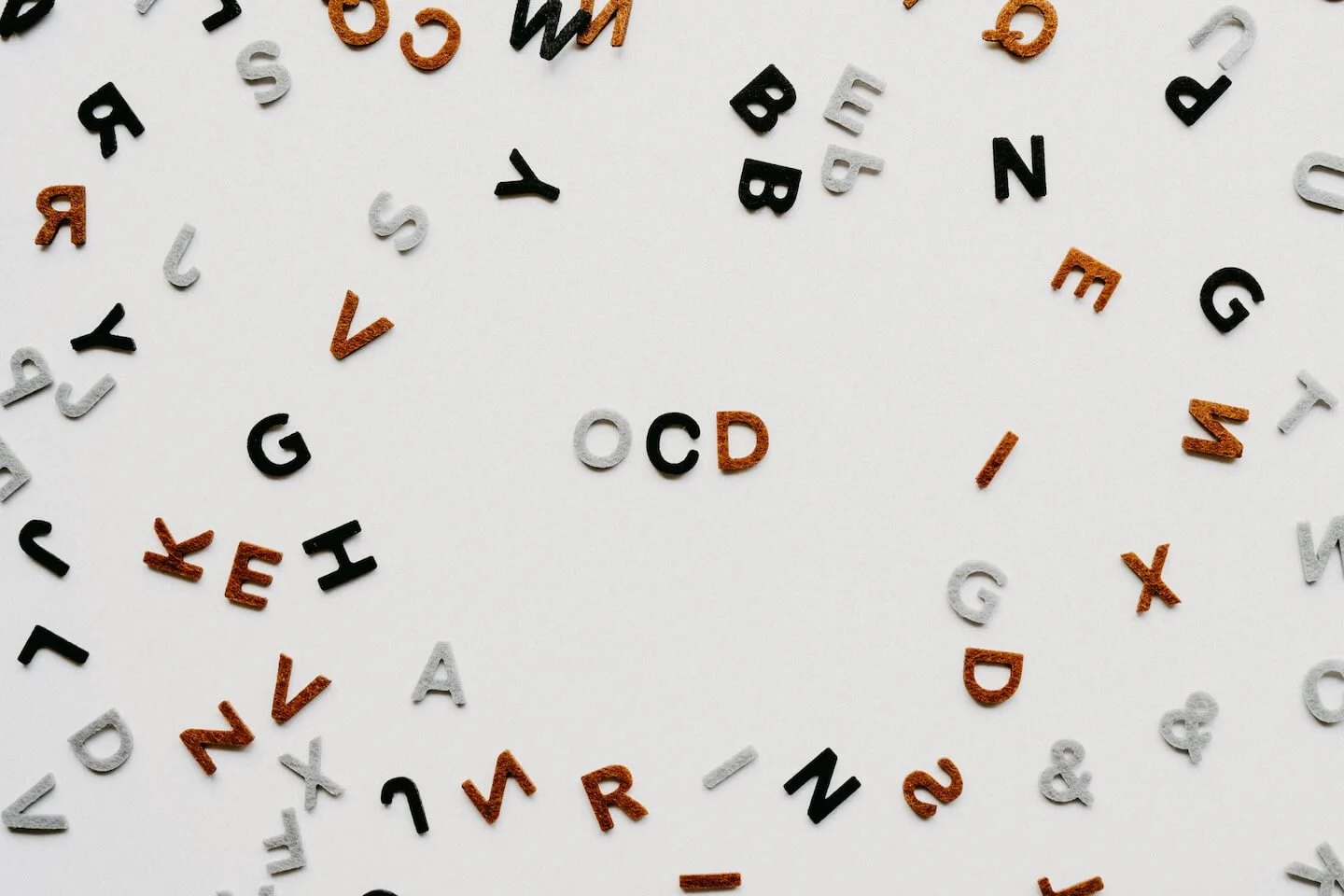 Letras sueltas de distintos colores colocadas de forma desordenada sobre fondo claro, formando un círculo irregular con la palabra OCD en el centro, transmitiendo sensación de confusión y repetición mental