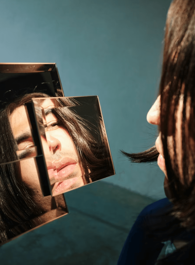 Persona observando su reflejo en un espejo fragmentado, creando una imagen dividida del rostro