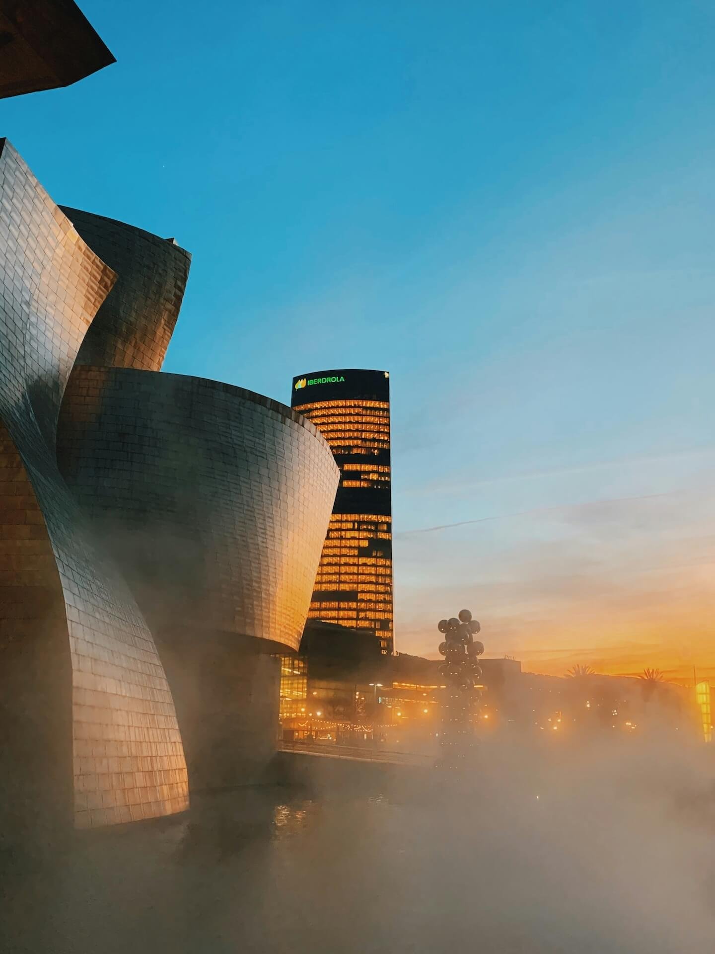 El guggenheim de bilbao con la torre iberdrola de fondo en un atardecer en la hora dorada