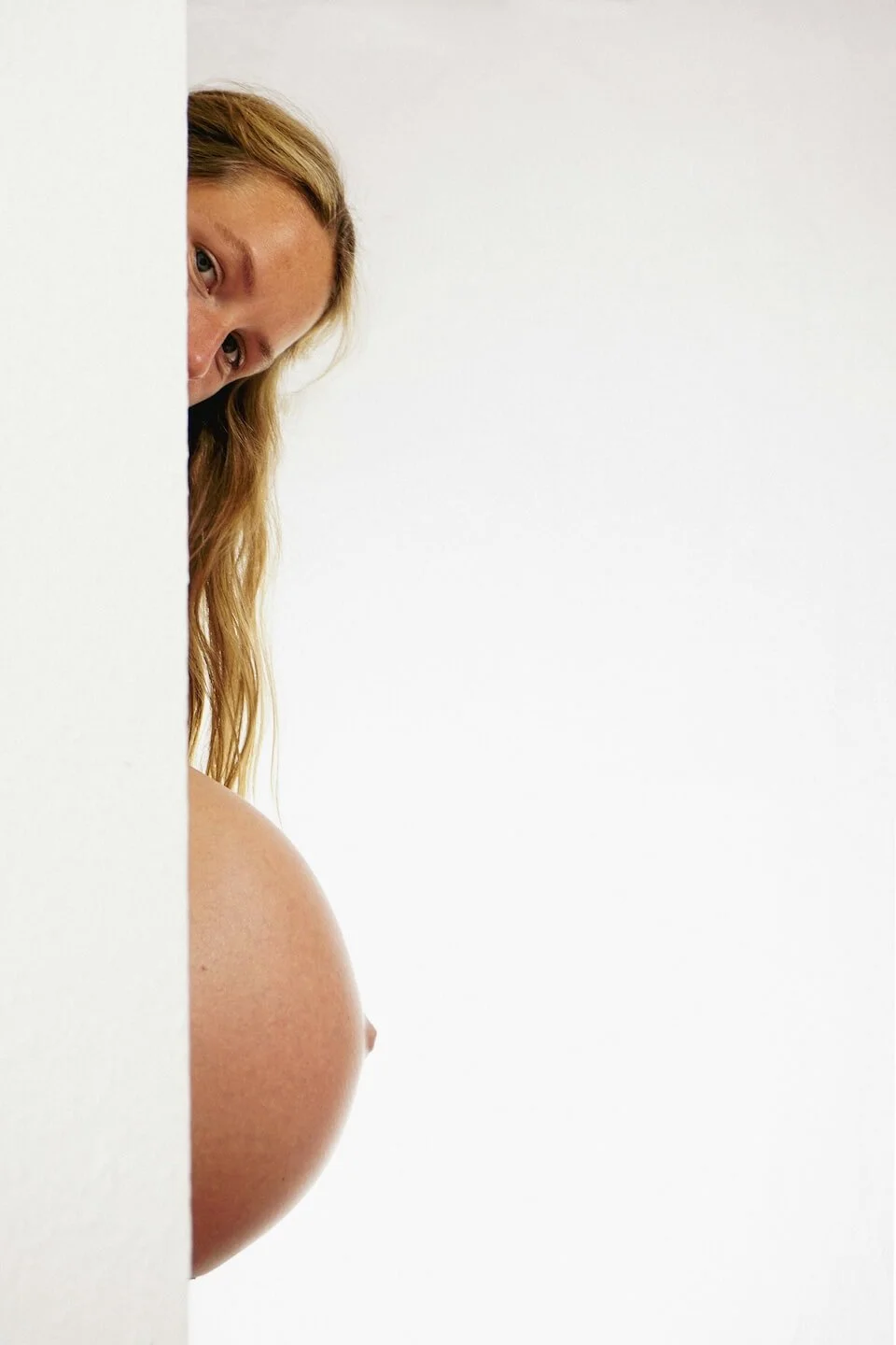 mujer embarazada de perfil tras una pared blanca