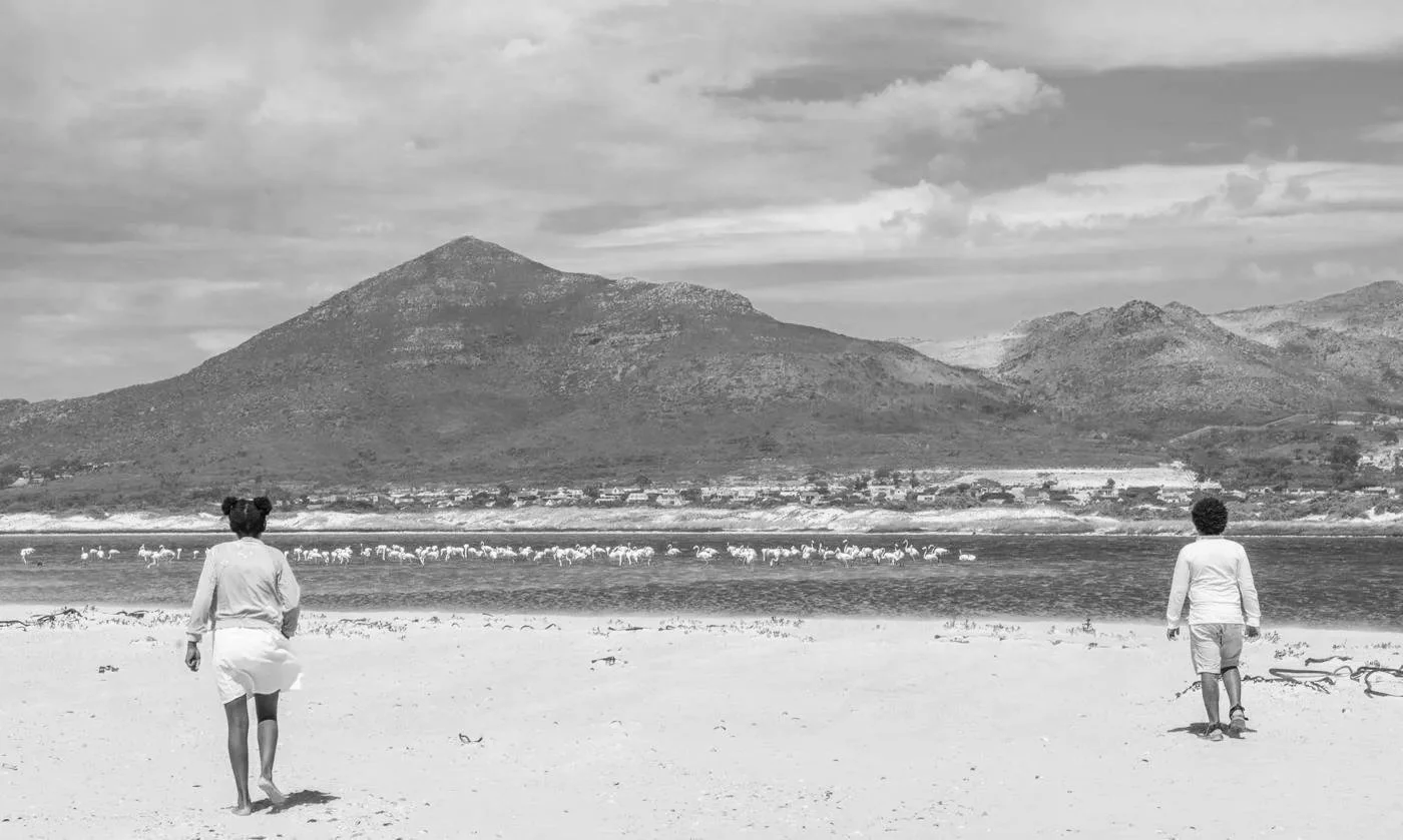 Twee kinderen lopen op een zandstrand met een meer en een berglandschap op de achtergrond.
