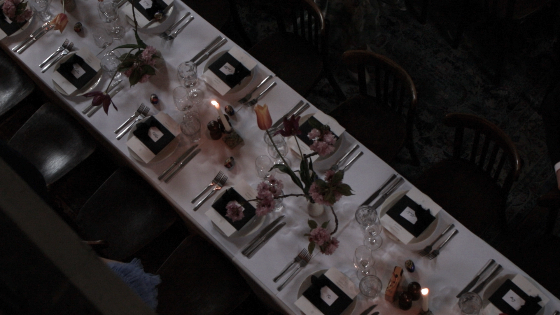 A long dining table set for a wedding dinner at Sessions Arts Club with pink flowers and candles as centerpieces, multiple glasses and silverware at each place setting, and black and white menu cards.