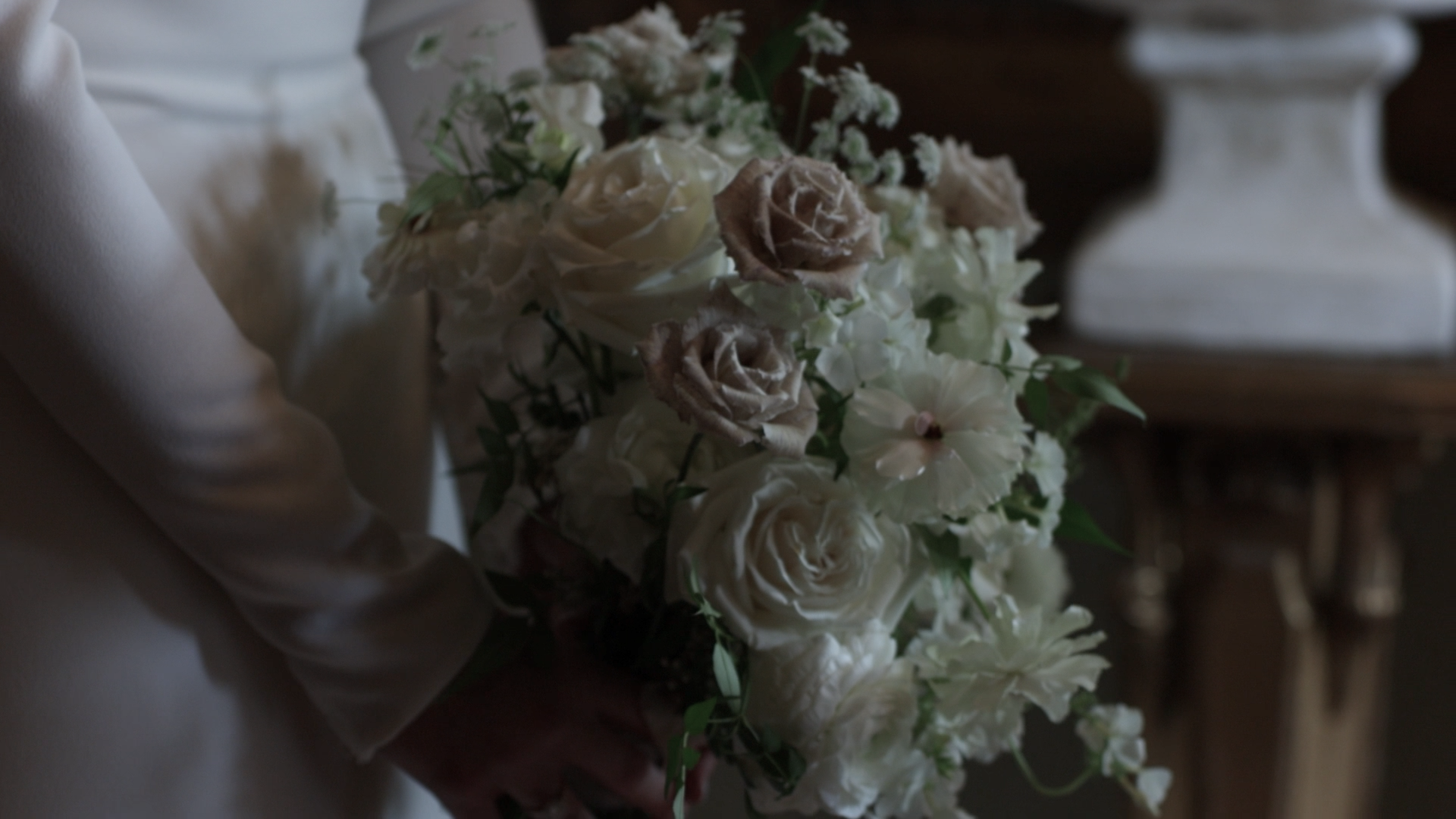 Person holding a bouquet of white and beige roses and other flowers at a London wedding.