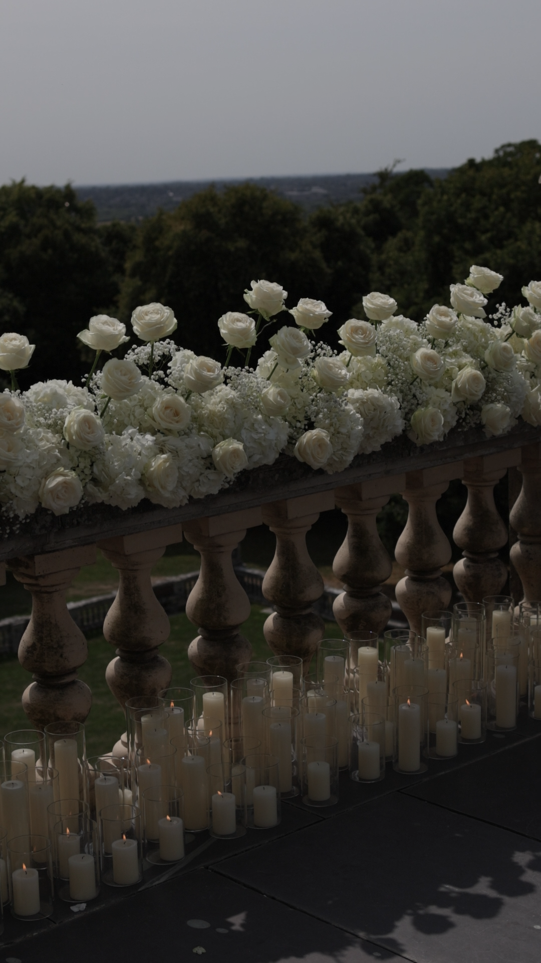 White floral arrangement on a wooden railing with candles below, overlooking the grounds at Cliveden House.