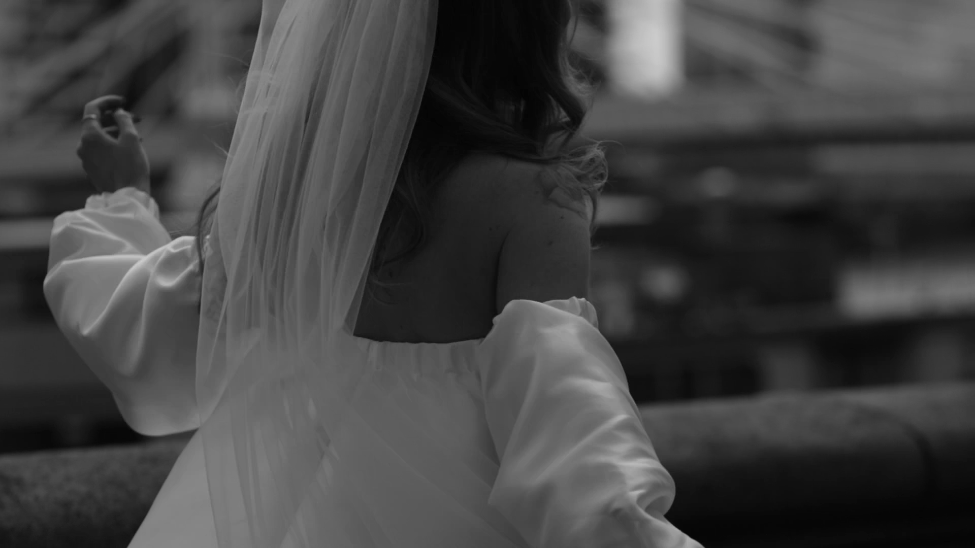 A woman wearing a wedding dress and veil twirling beside Chelsea embankment, turned away from the camera with a blurred background.