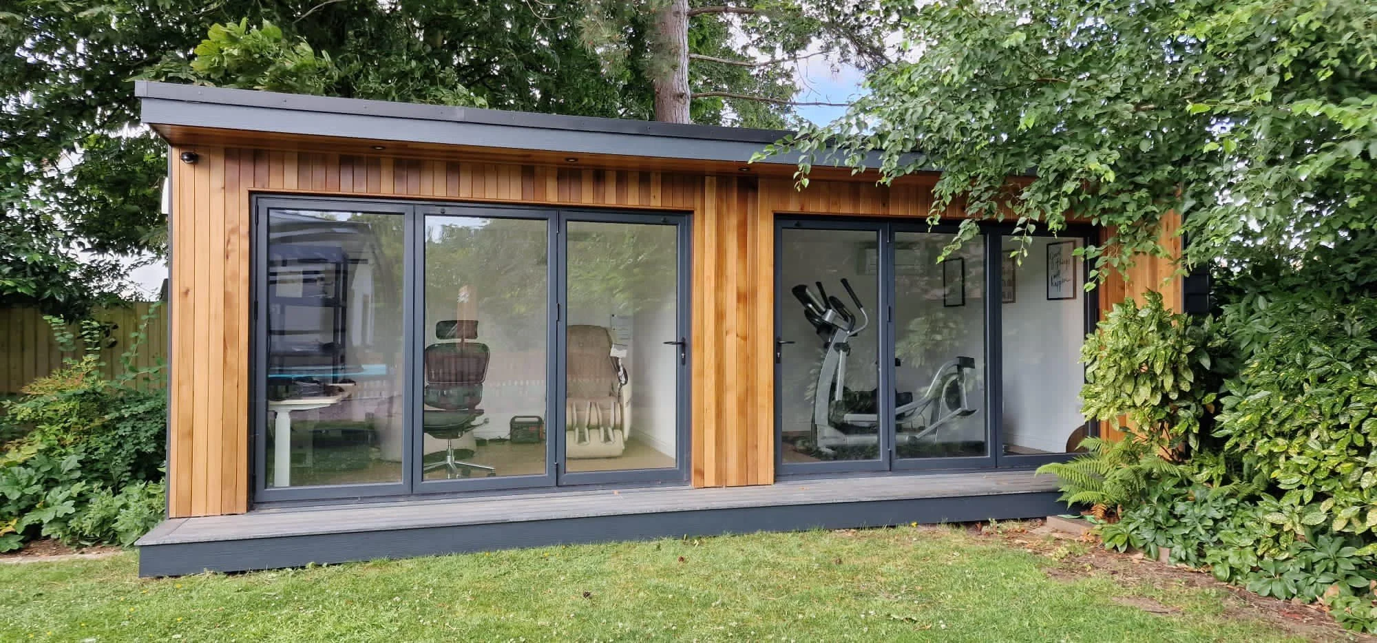 Small modern backyard gym and office with large glass sliding doors, surrounded by greenery.
