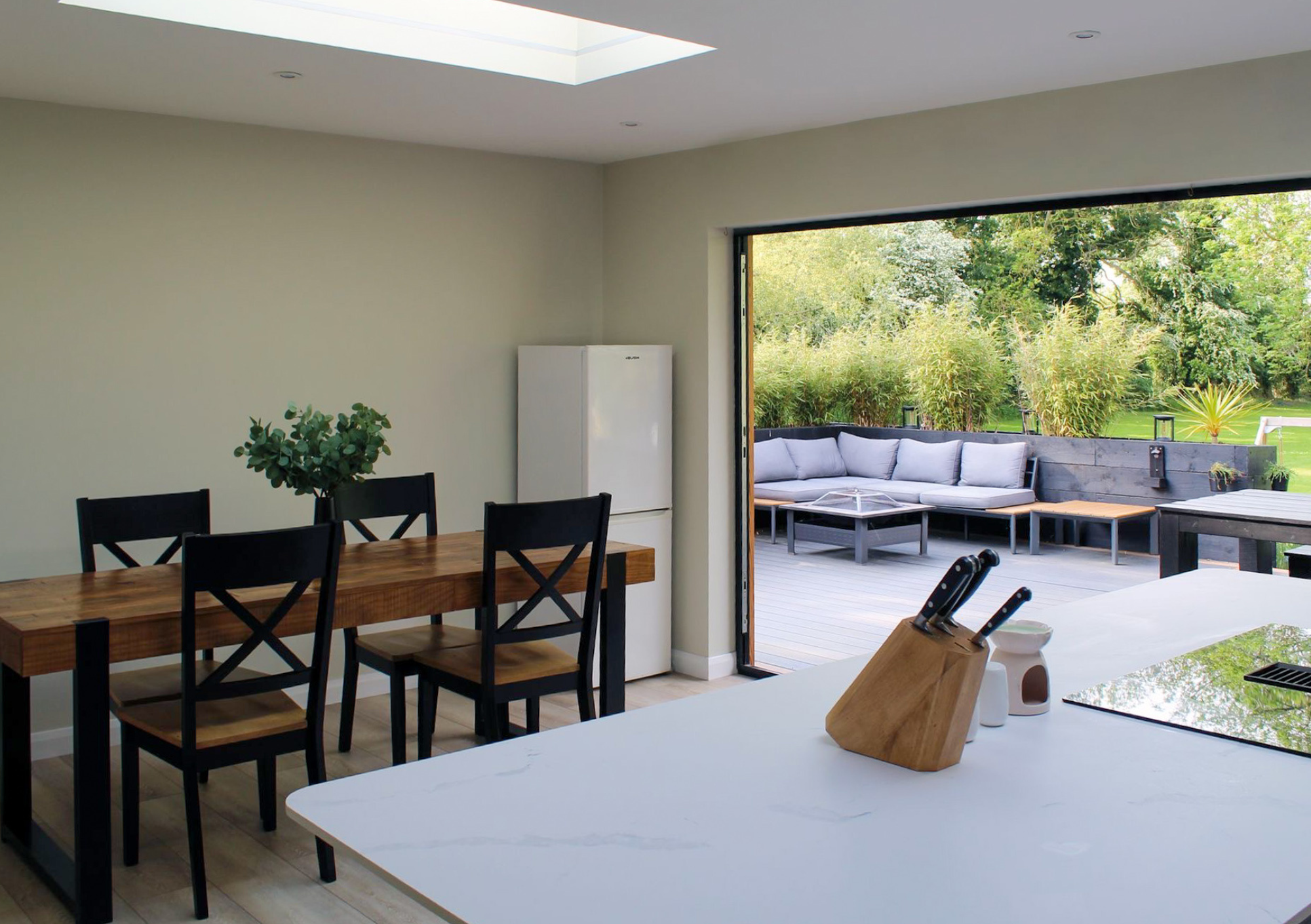 View of a modern open-concept kitchen and dining area with a sliding glass door leading to an outdoor patio with seating and greenery.