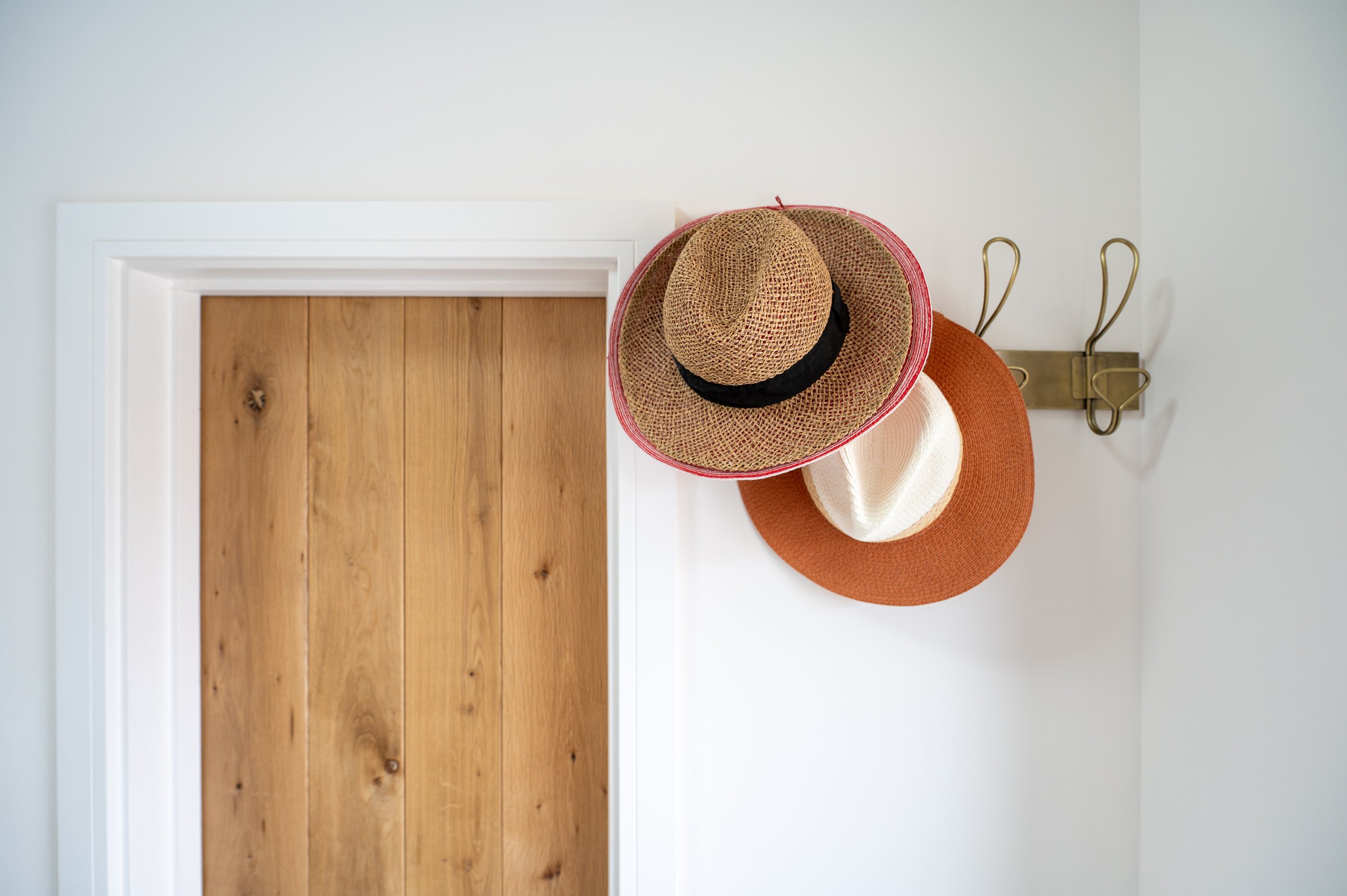 Three hats hanging on a wall hook above a wooden door, with a white wall background.