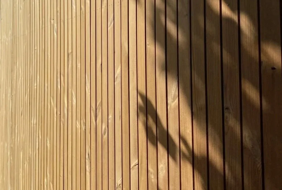 Close-up view of wooden slats on a wall with shadows cast across them.