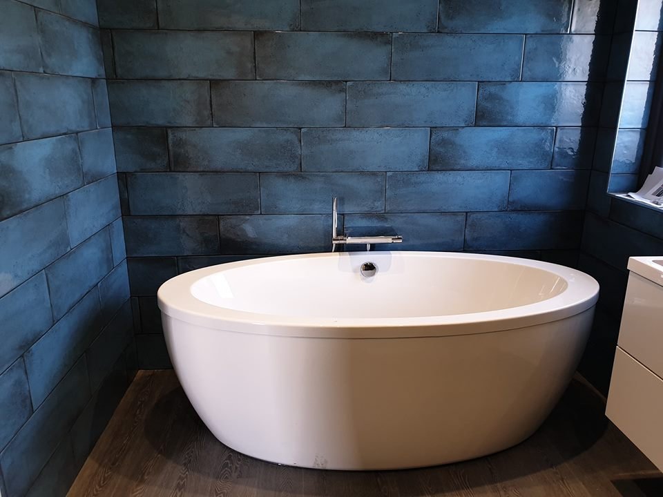 Freestanding white bathtub in a modern bathroom with blue tiled walls and a wooden floor.
