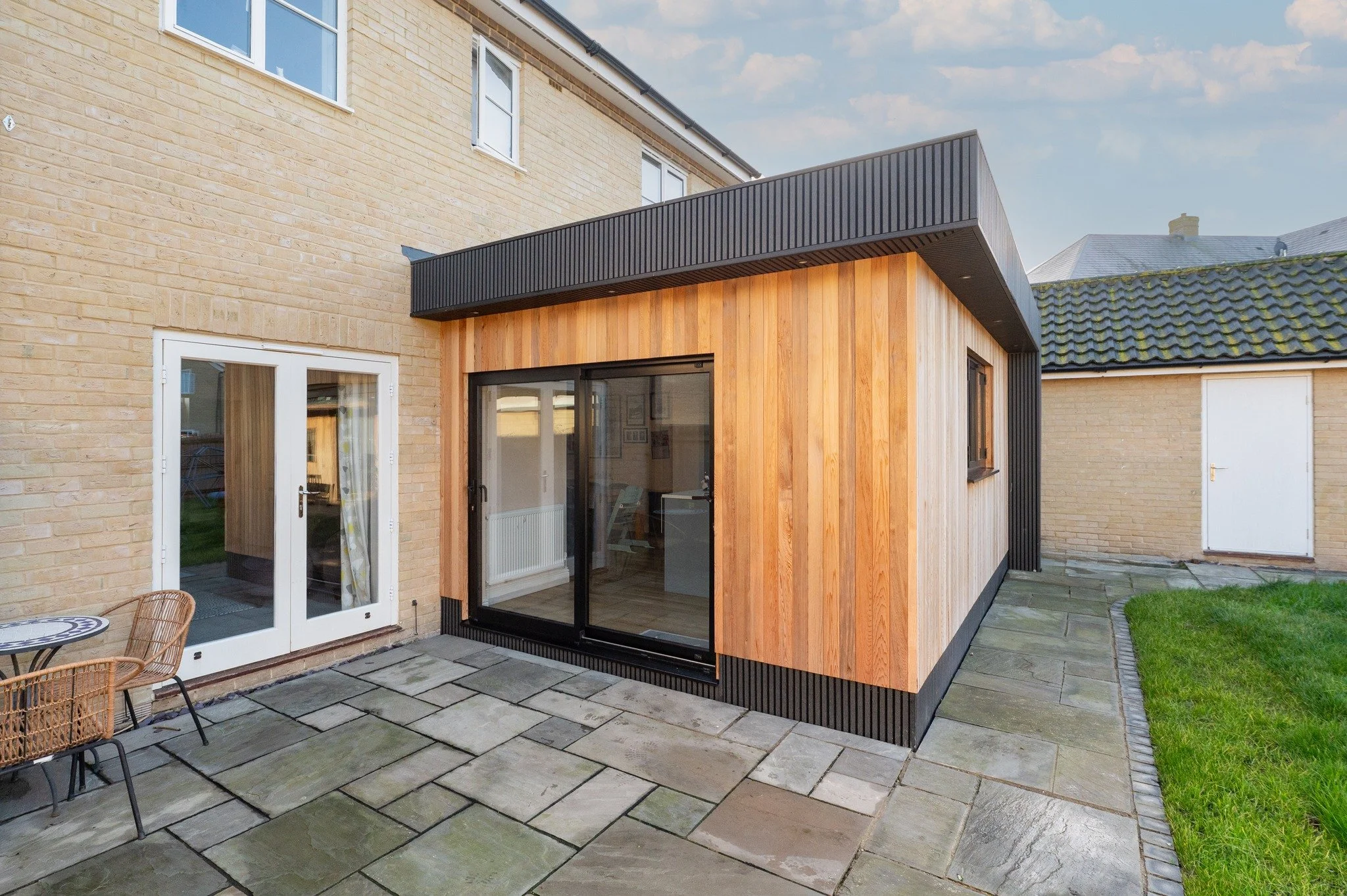 Backyard with brick and wood addition, sliding glass door, patio furniture, and surrounding grass and paving stones.