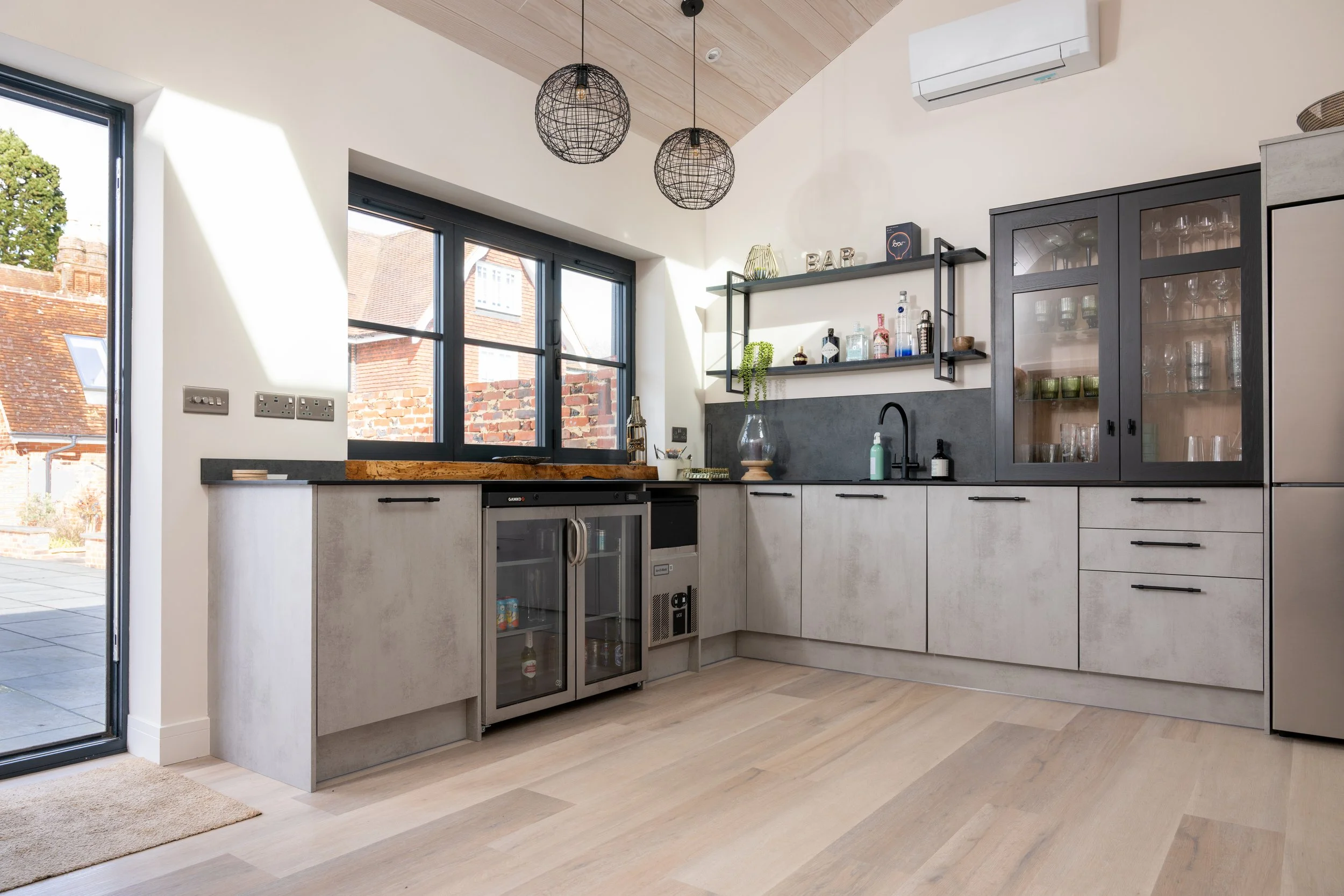 Modern kitchen with concrete cabinets, black hardware, open shelving, and large windows letting in natural light.