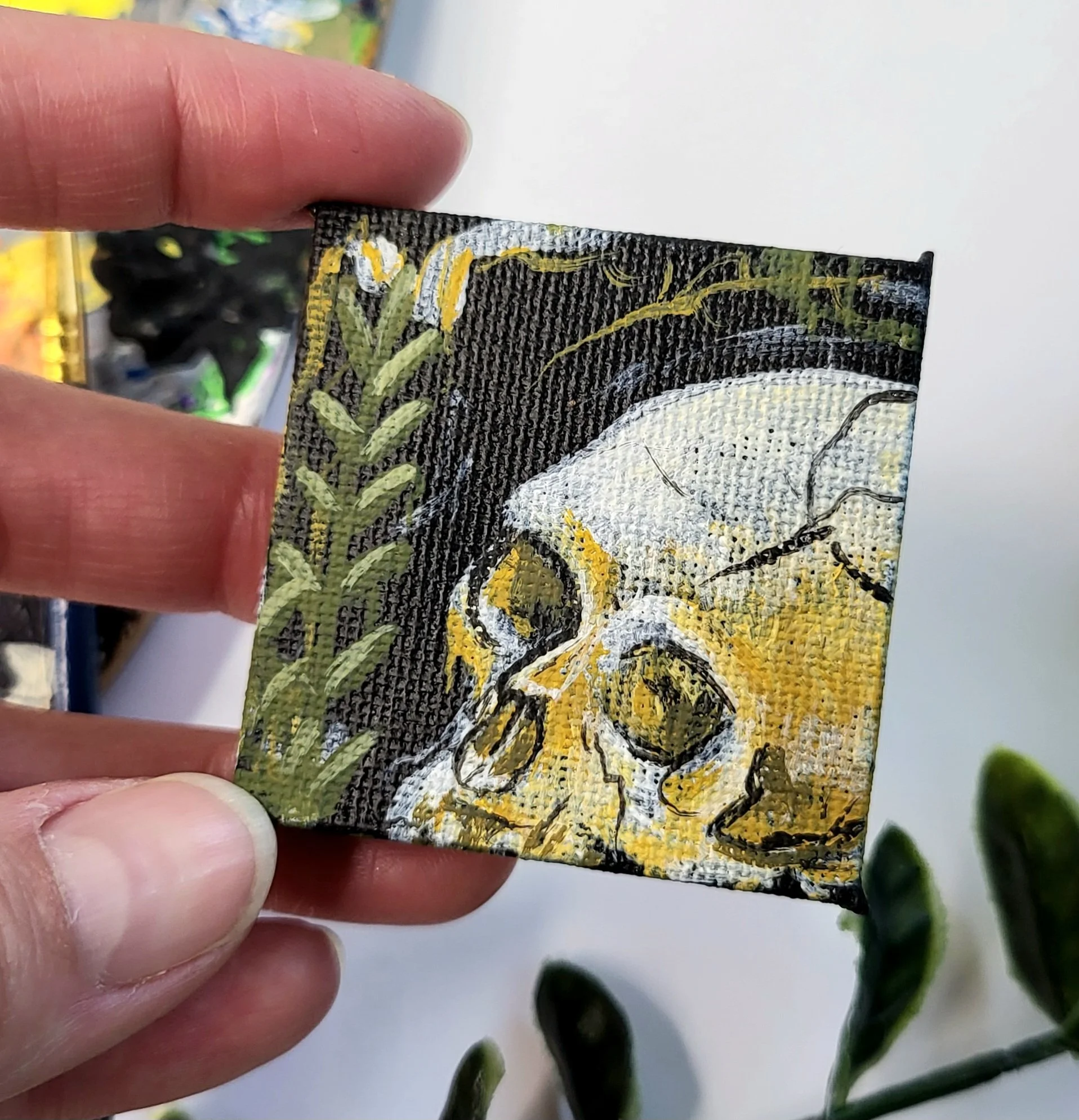 Close-up of a hand holding a small, rectangular object with intricate artwork depicting a leopard's face surrounded by green leaves, set against a blurred background.