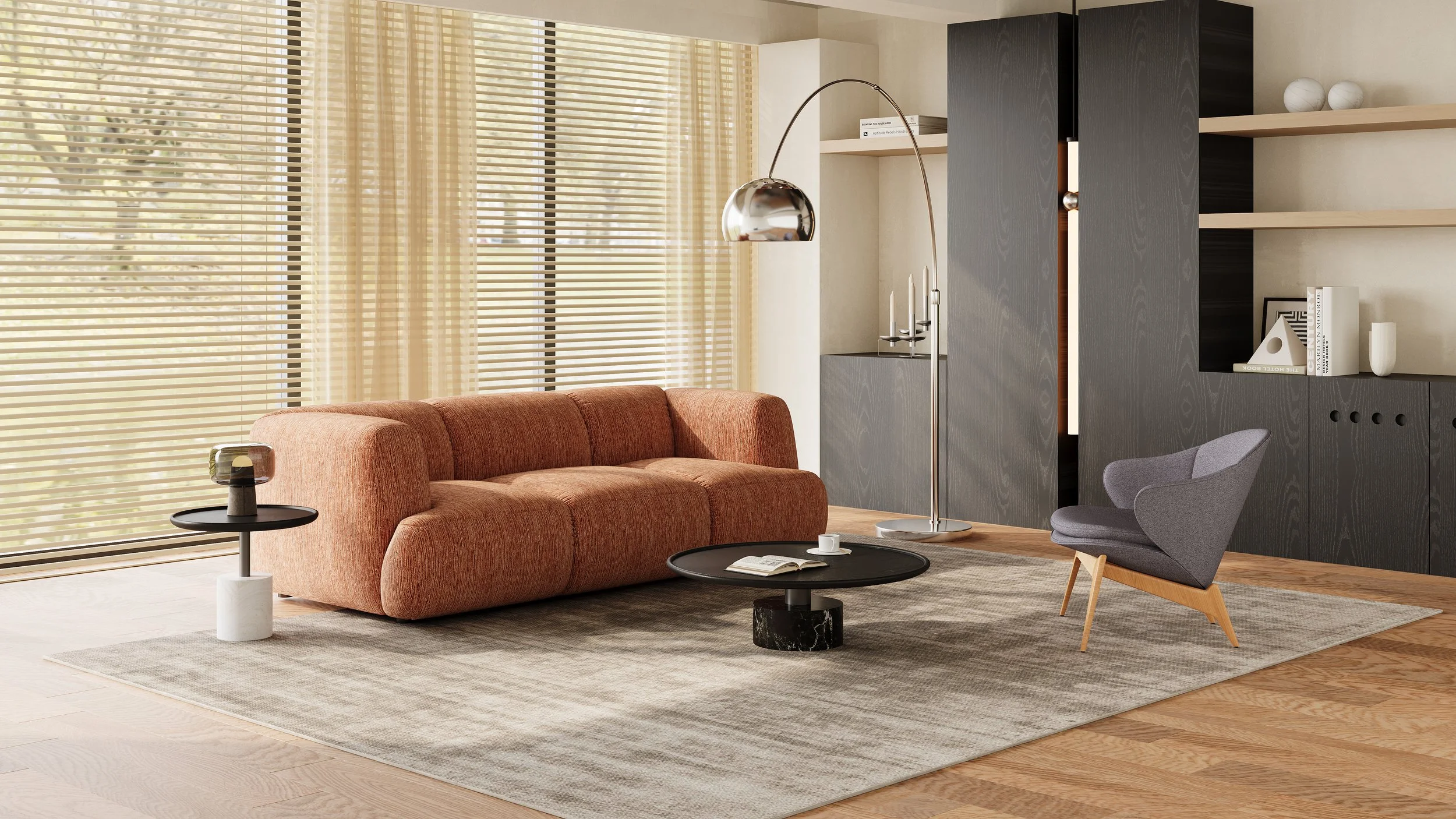 Living room with a Nest Space coral sofa, a grey armchair, and black and white coffee tables. Large windows with beige blinds, wooden flooring, and minimal decor.