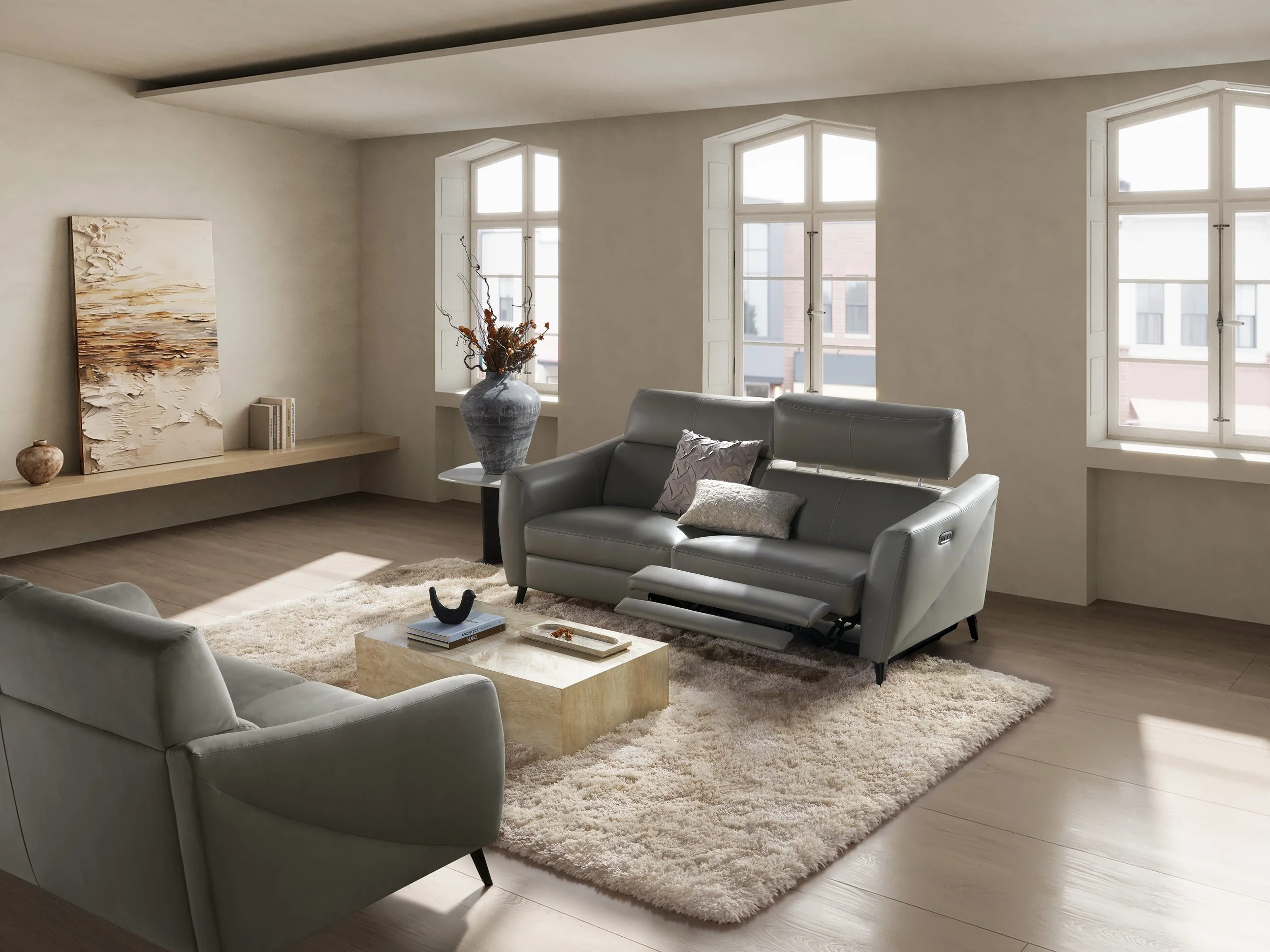 Living room with beige walls, large windows, grey Nest Space leather sofas, a beige shag rug, a coffee table with decorative items, and a ledge with artwork and vases.