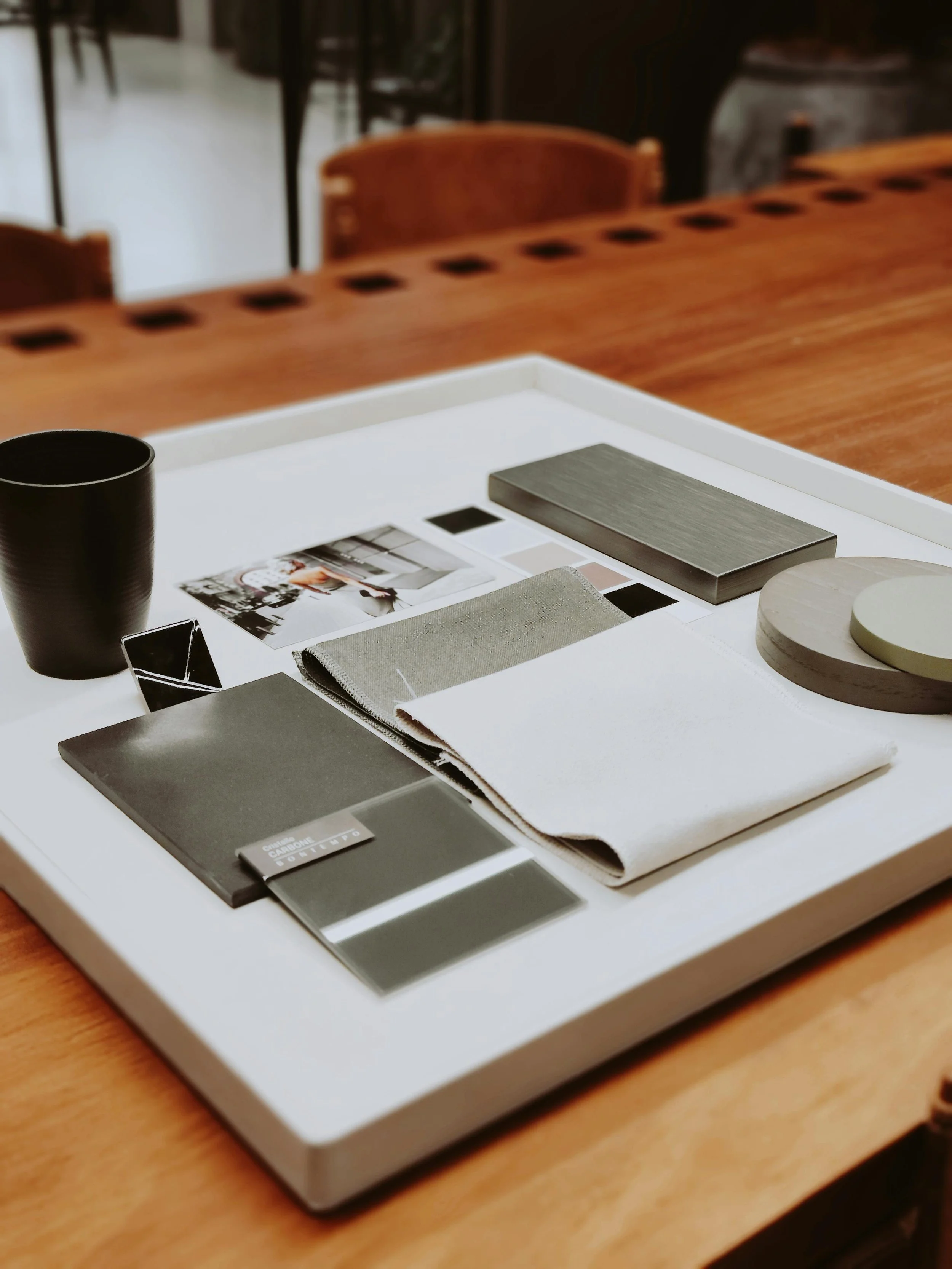Design and interior color palette presentation on a white tray, including fabric swatches, paint chips, and color samples, placed on a wooden table.