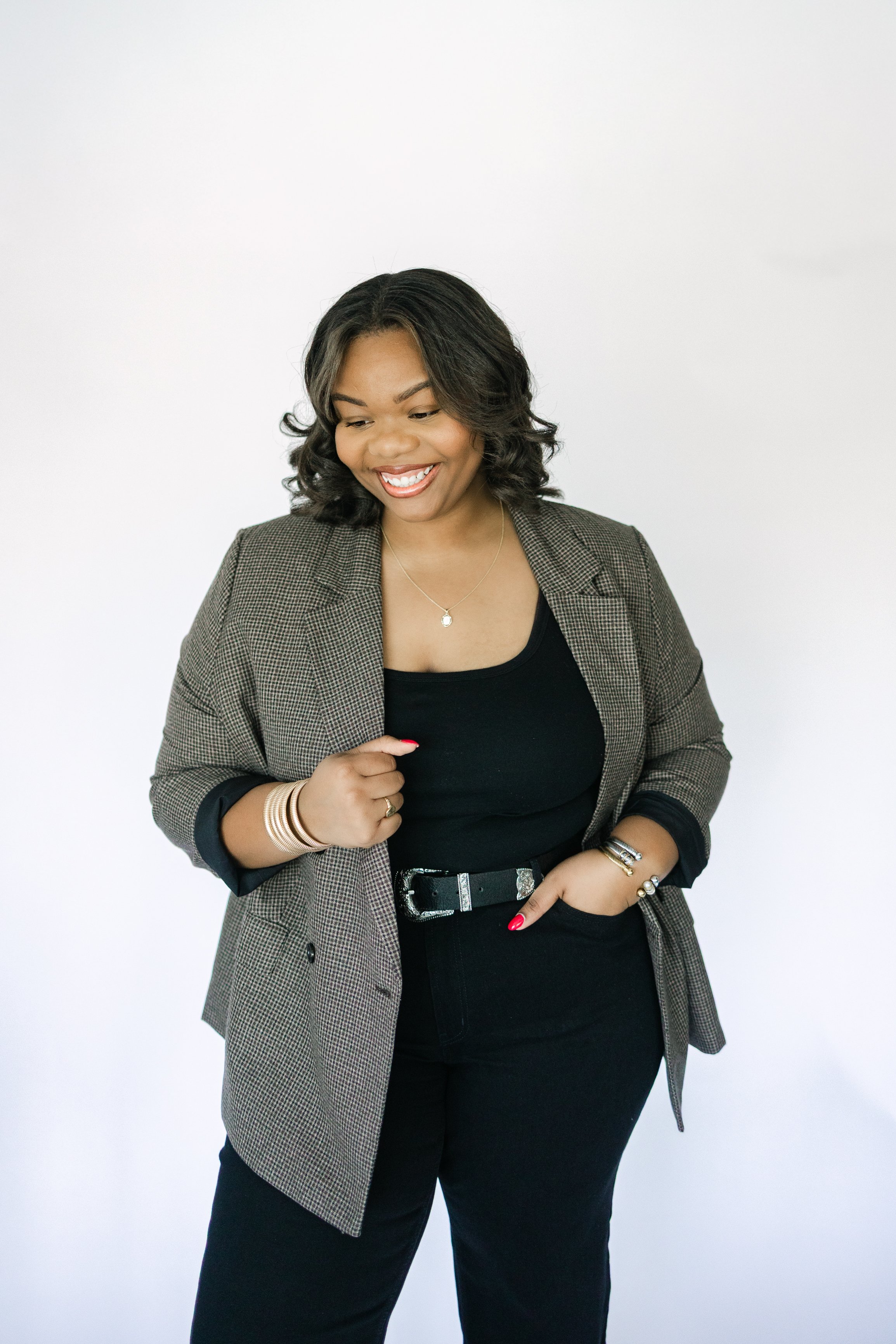 Smiling woman wearing a blazer and black outfit, standing against a white background.