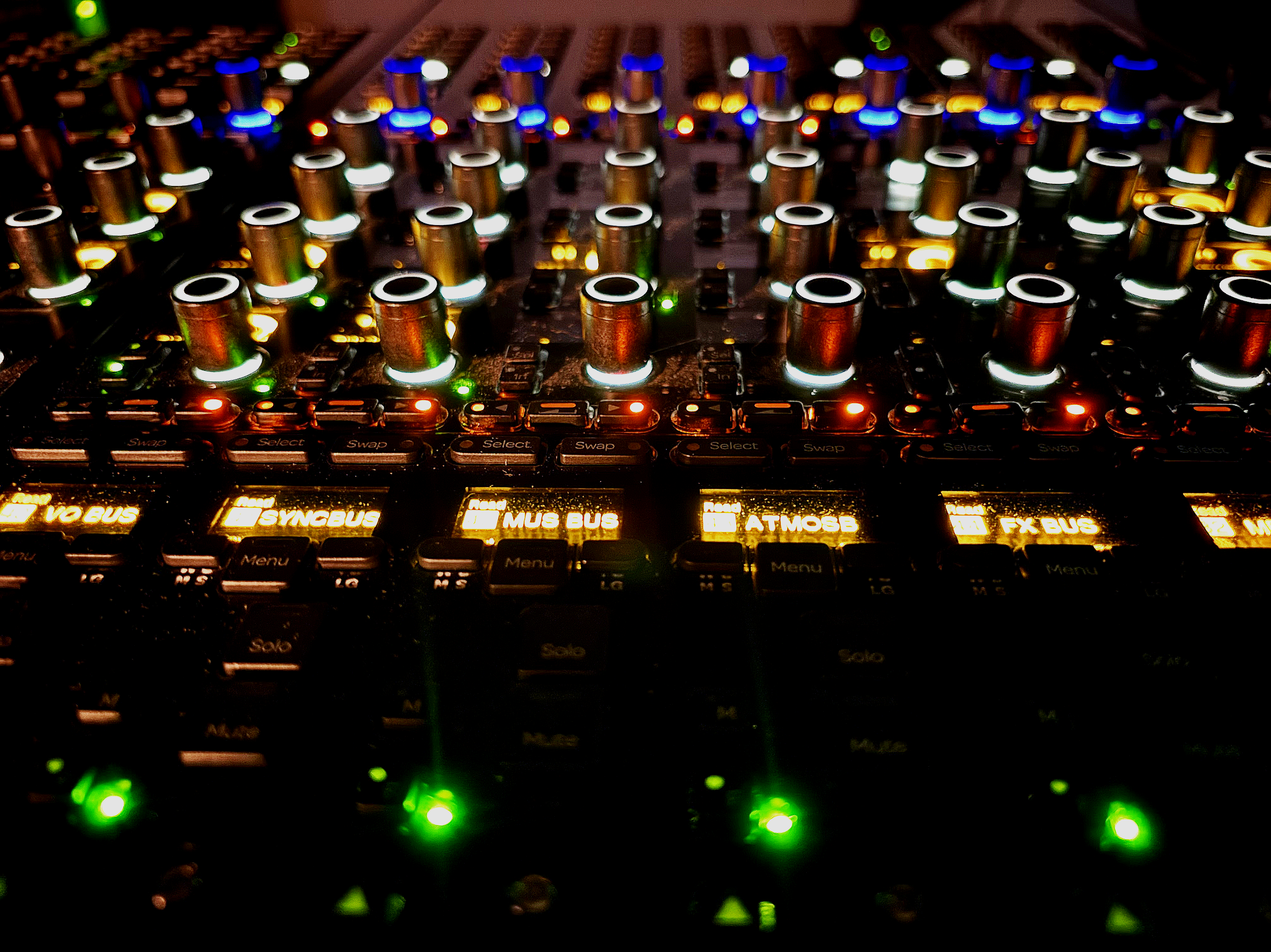 A close-up view of a professional mixing desk with illuminated buttons and knobs, displaying colourful LED lights.