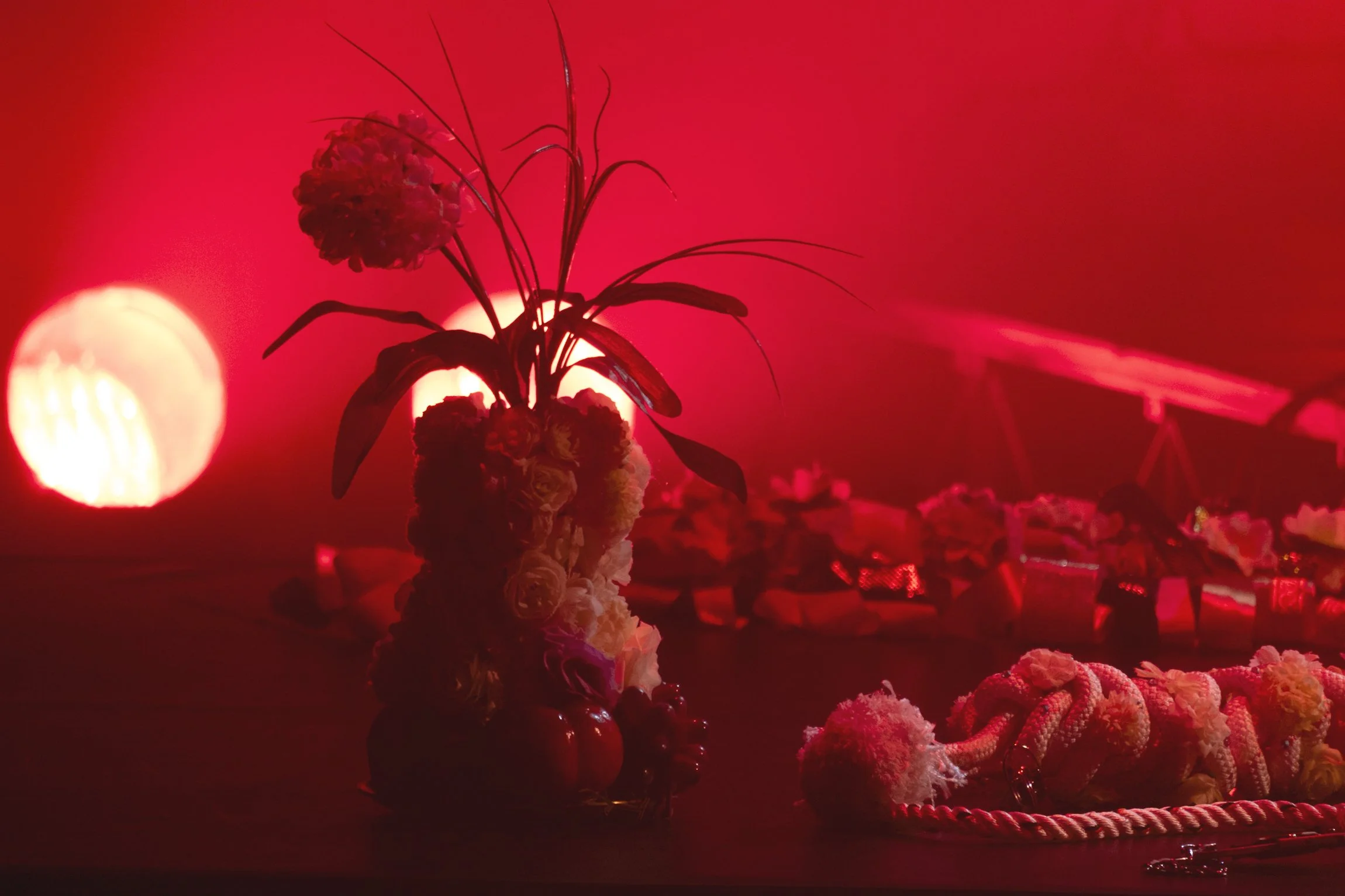 A floral arrangement with a red background, illuminated by soft, red lighting, featuring various flowers and decorative elements on a table or surface.