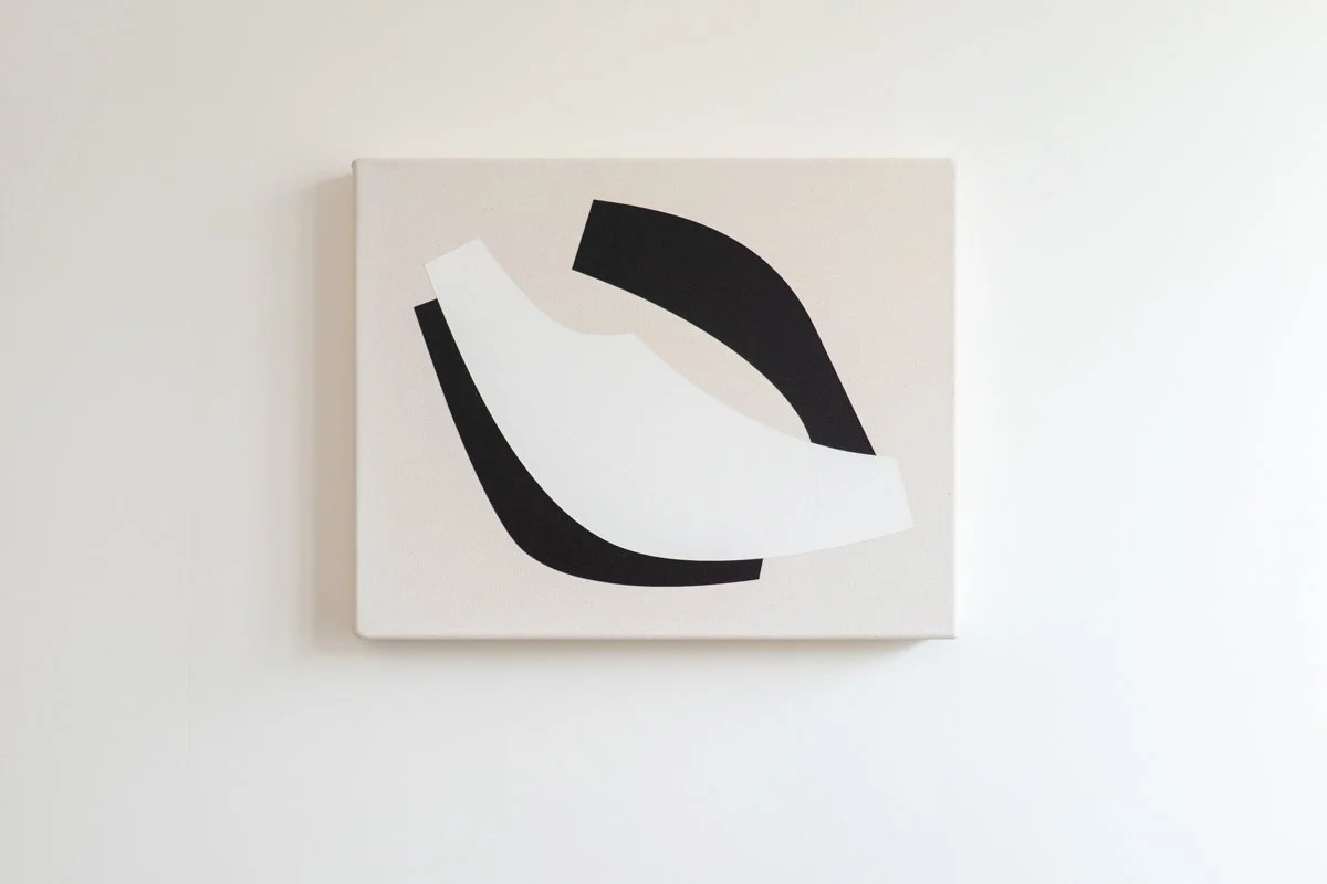 Abstract black and white geometric artwork on a white canvas mounted on a white wall.