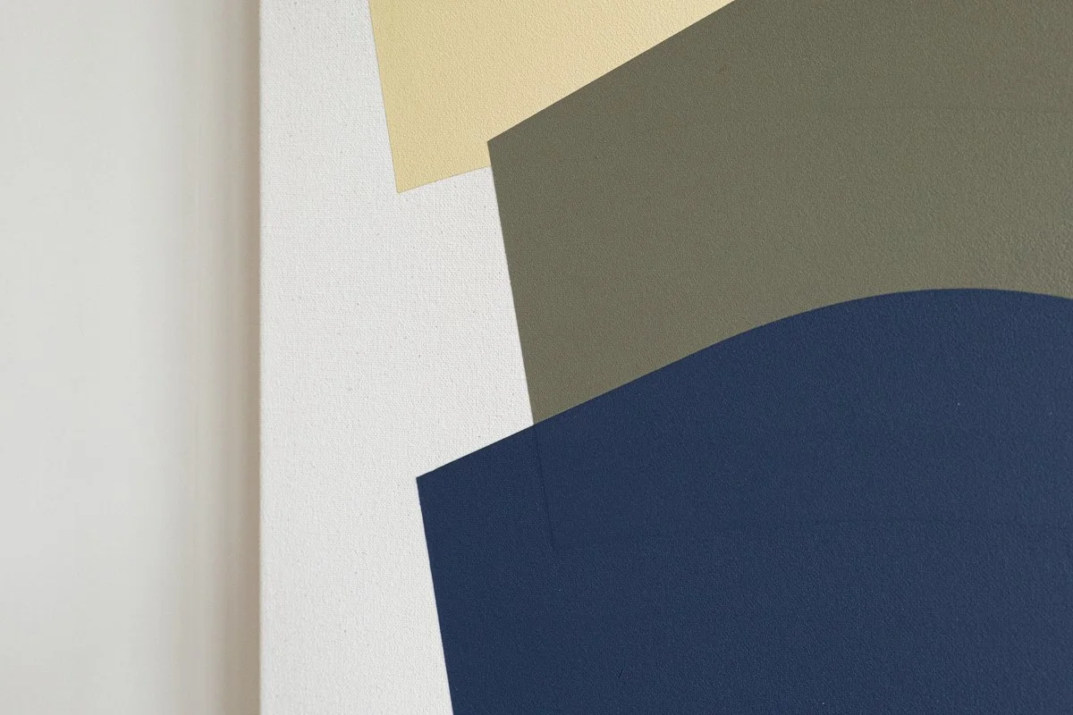 Close-up of a geometric abstract art piece with overlapping shapes in beige, green, white, and navy blue on a wall.