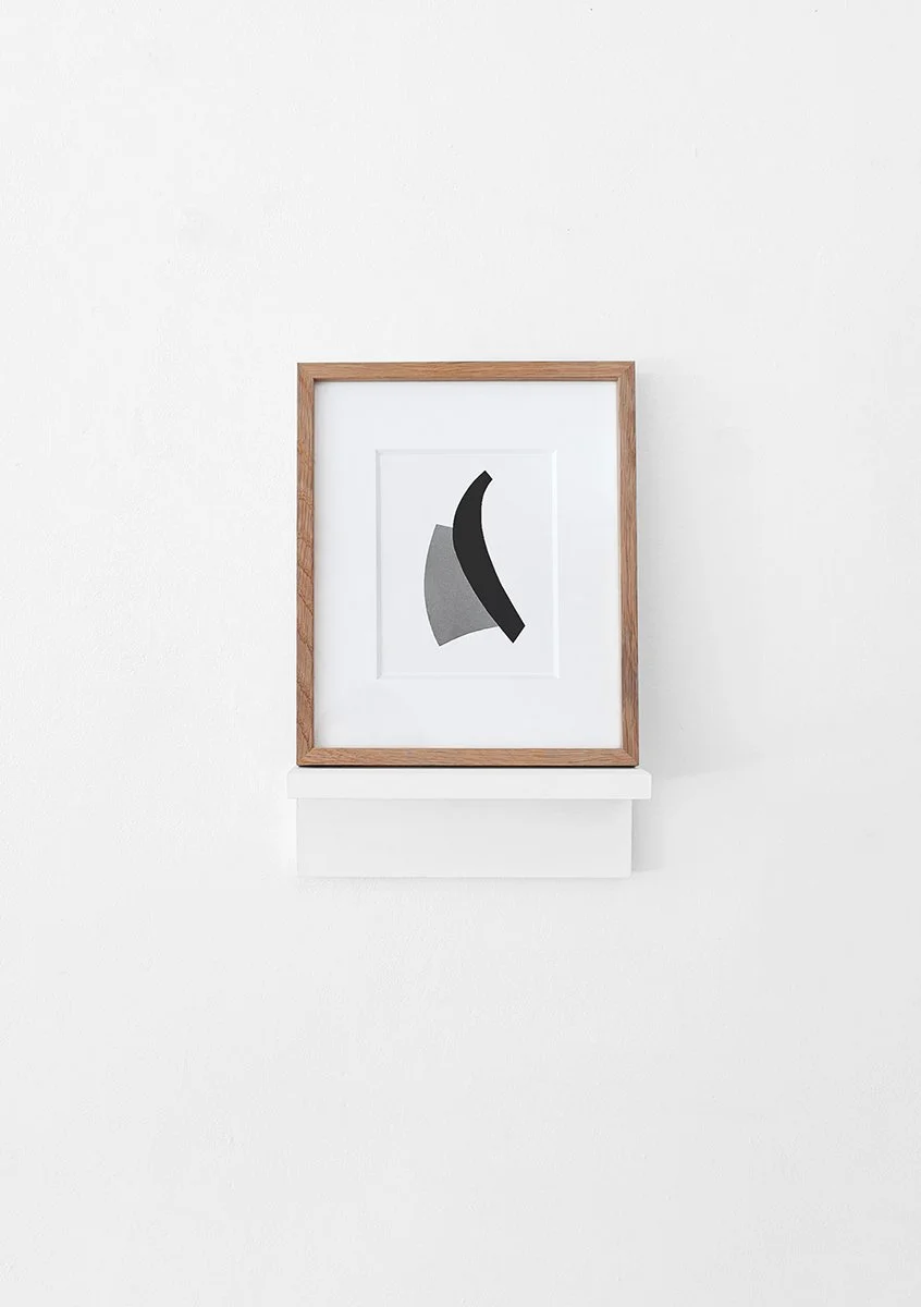 Minimalist abstract artwork in a wooden frame on a white wall.