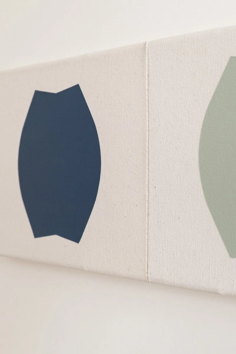 Close-up of a white canvas wall art with abstract shapes in navy and light green, hung on a white wall.