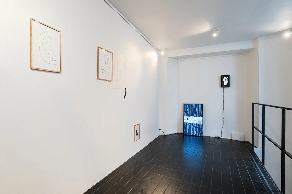 Contemporary art gallery with white walls, black tile floor, and several minimalist artworks including framed line drawings and illuminated digital art pieces.