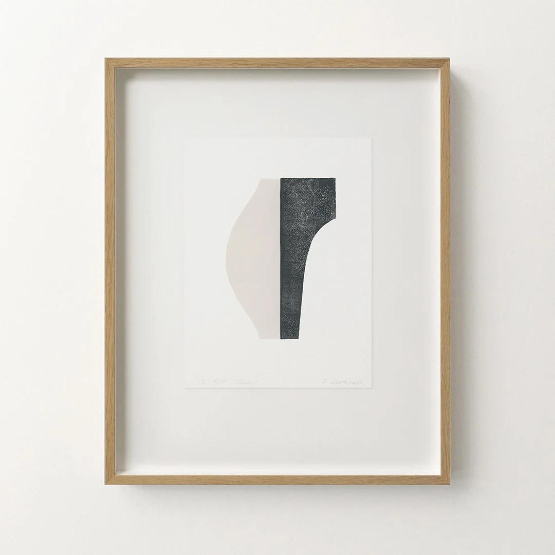 Minimalist black and white abstract artwork framed in light wood, displayed on a white wall.