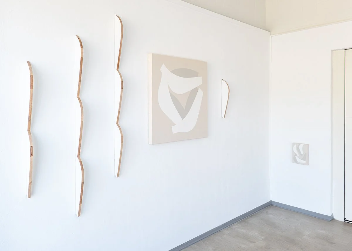 Minimalist interior with abstract wall art and wooden wave-shaped wooden installation pieces on a white wall.