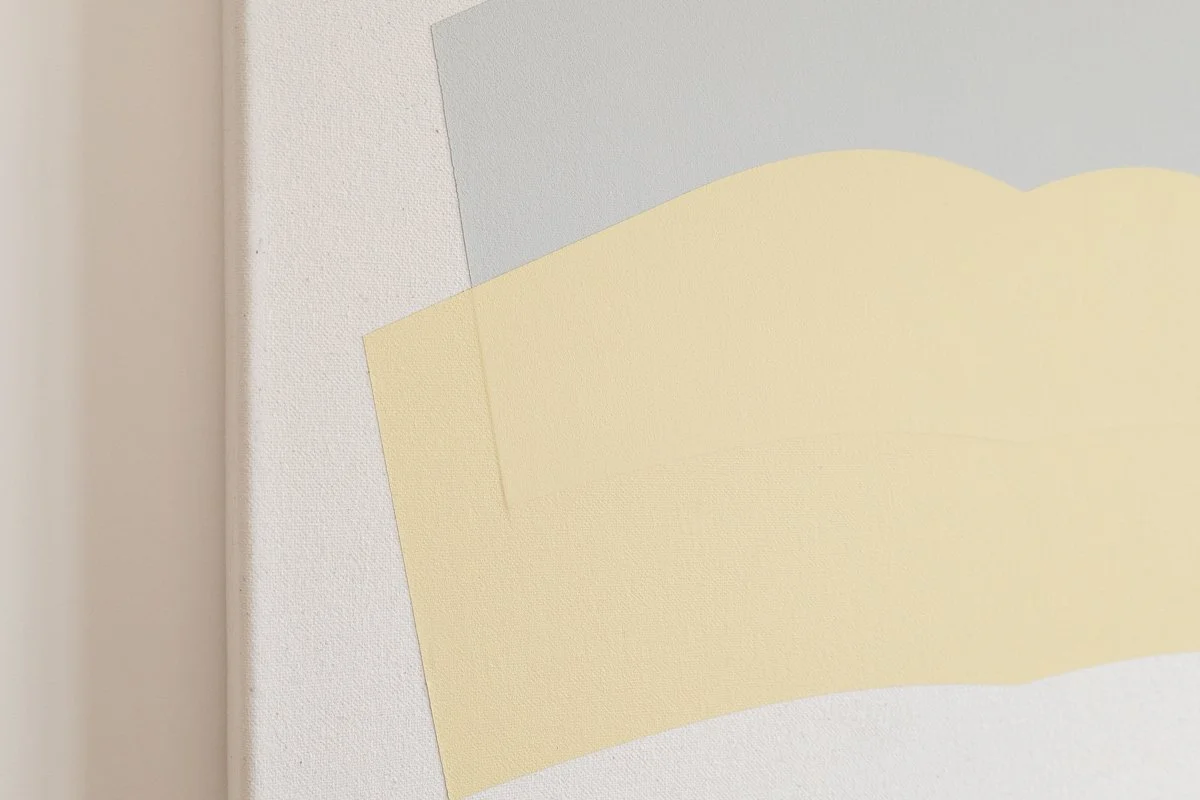 Close-up of abstract paper art with overlapping pastel-colored paper sheets in shades of cream, light yellow, and gray.