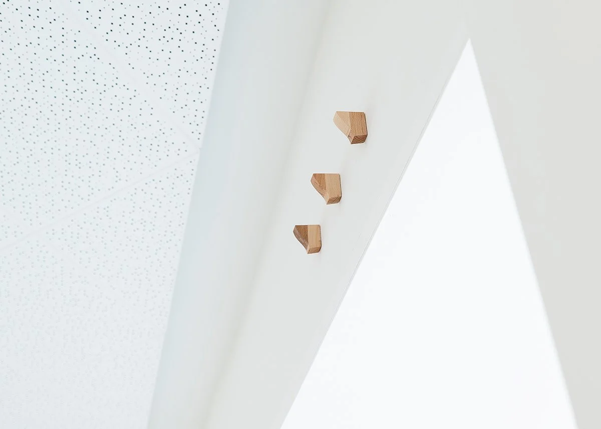 Close-up of a white wall with three small, angled wooden installation pieces mounted on it.