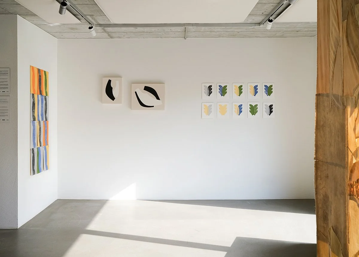 Art gallery with abstract paintings on white walls, featuring various shapes and colors including black, blue, green, yellow, and orange.