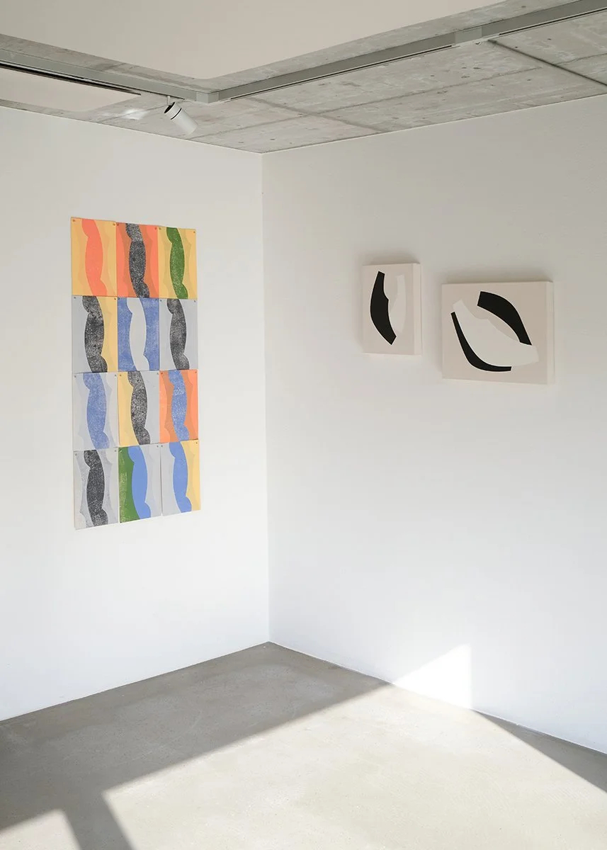 Art exhibition with colorful abstract lino prints on the left and two black and white minimalist paintings on the right corner of a white wall by Tetiana Kartasheva, Zurich, Switzerland. Exhibited in Laax.