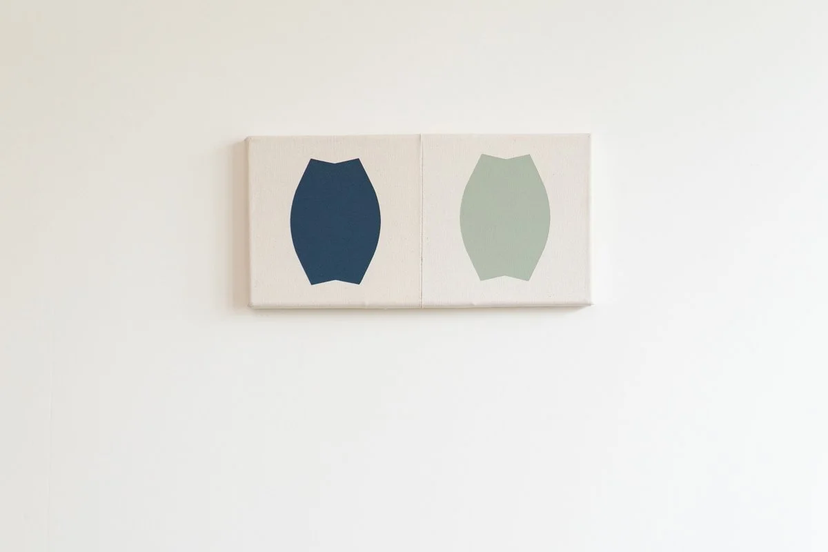 Two minimalist paintings with abstract shapes in dark blue and light green, hung side by side on a white wall.