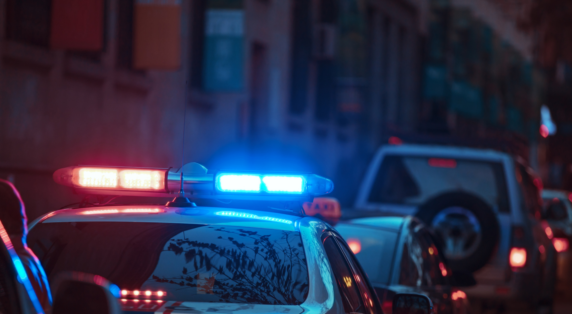 Coche de policía con luces azules y rojas encendidas, deteniéndose en medio de tráfico por la noche